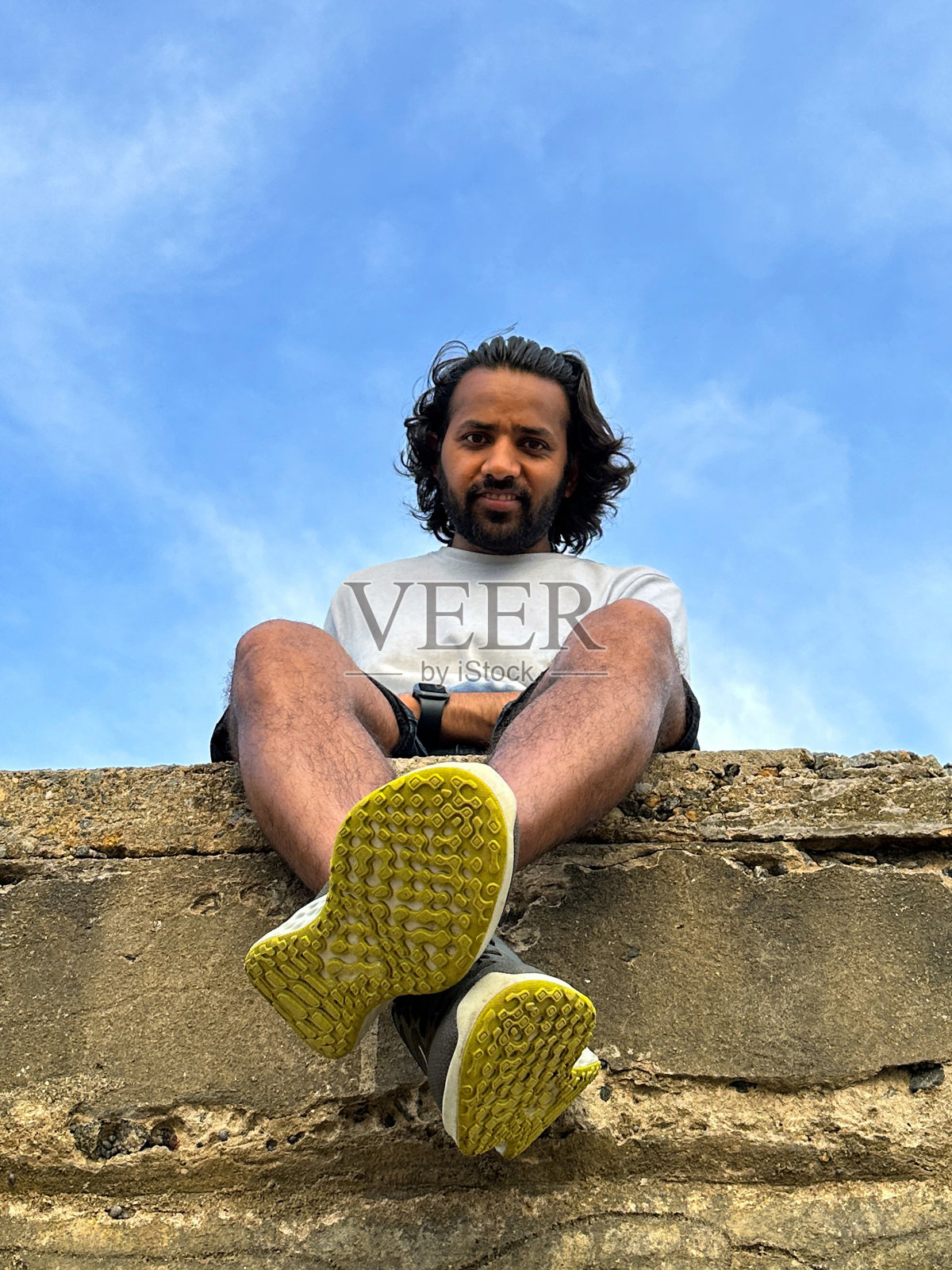 人坐在海岸海堤，混凝土防御，海岸管理的特写图像，向下看相机，多云的蓝色晴朗的天空背景，从下面看，重点在前景照片摄影图片