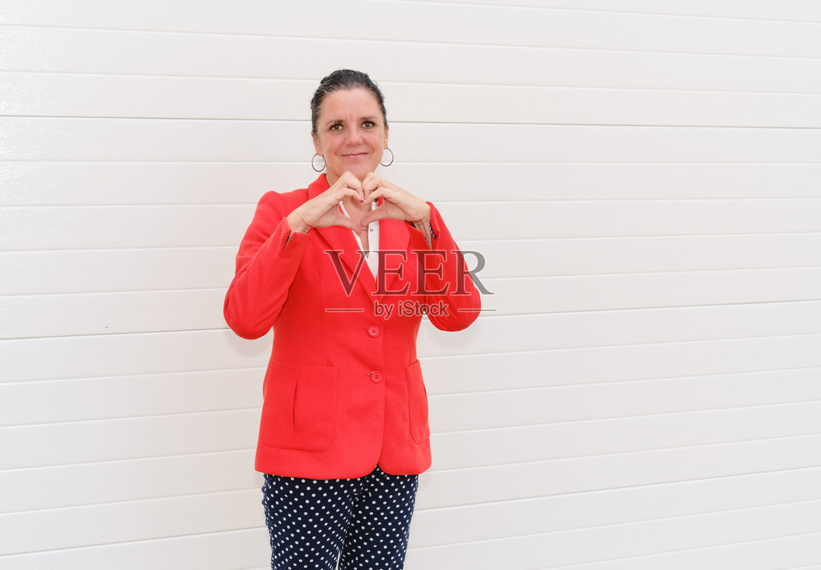 在白色的墙壁上，女人用双手做着心形的手势照片摄影图片