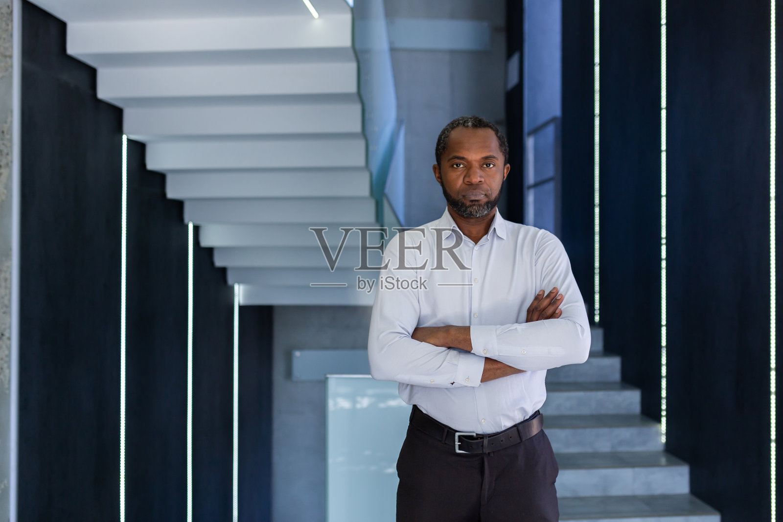 一个身穿白衬衫的非裔美国人站在办公中心，双臂交叉在胸前，自信而严肃地看着镜头照片摄影图片