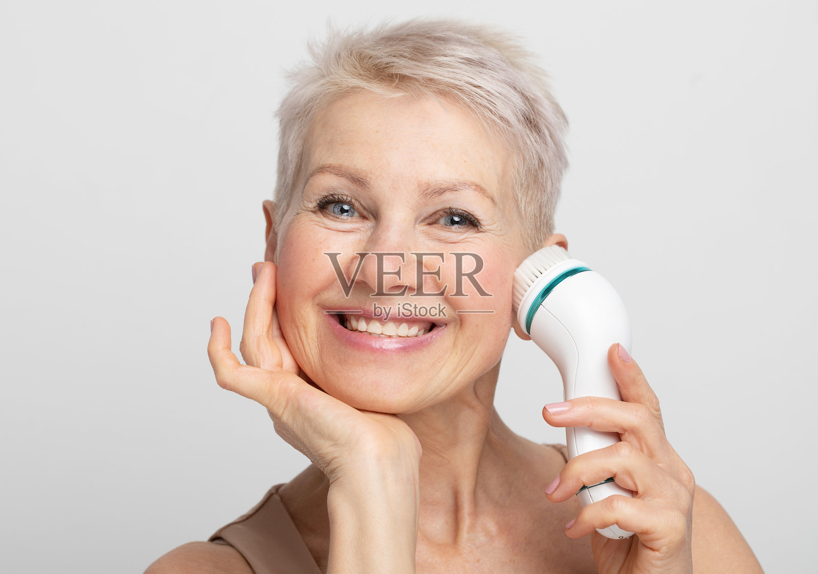 美丽的面孔肖像可爱和漂亮的高级妇女与短发使用面部按摩器完美的新鲜皮肤照片摄影图片