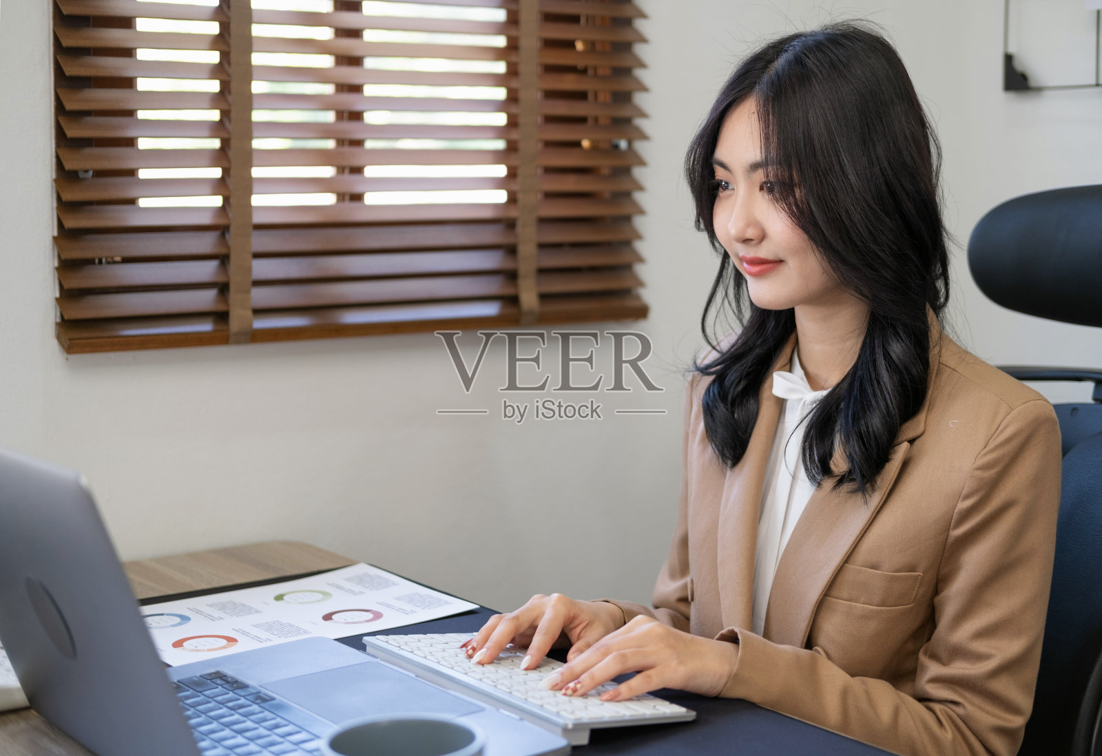 快乐的年轻女企业家用电脑看屏幕，在互联网上工作，坐在办公桌前，微笑的亚洲女性专业员工在工作场所的笔记本电脑上输入电子邮件。照片摄影图片