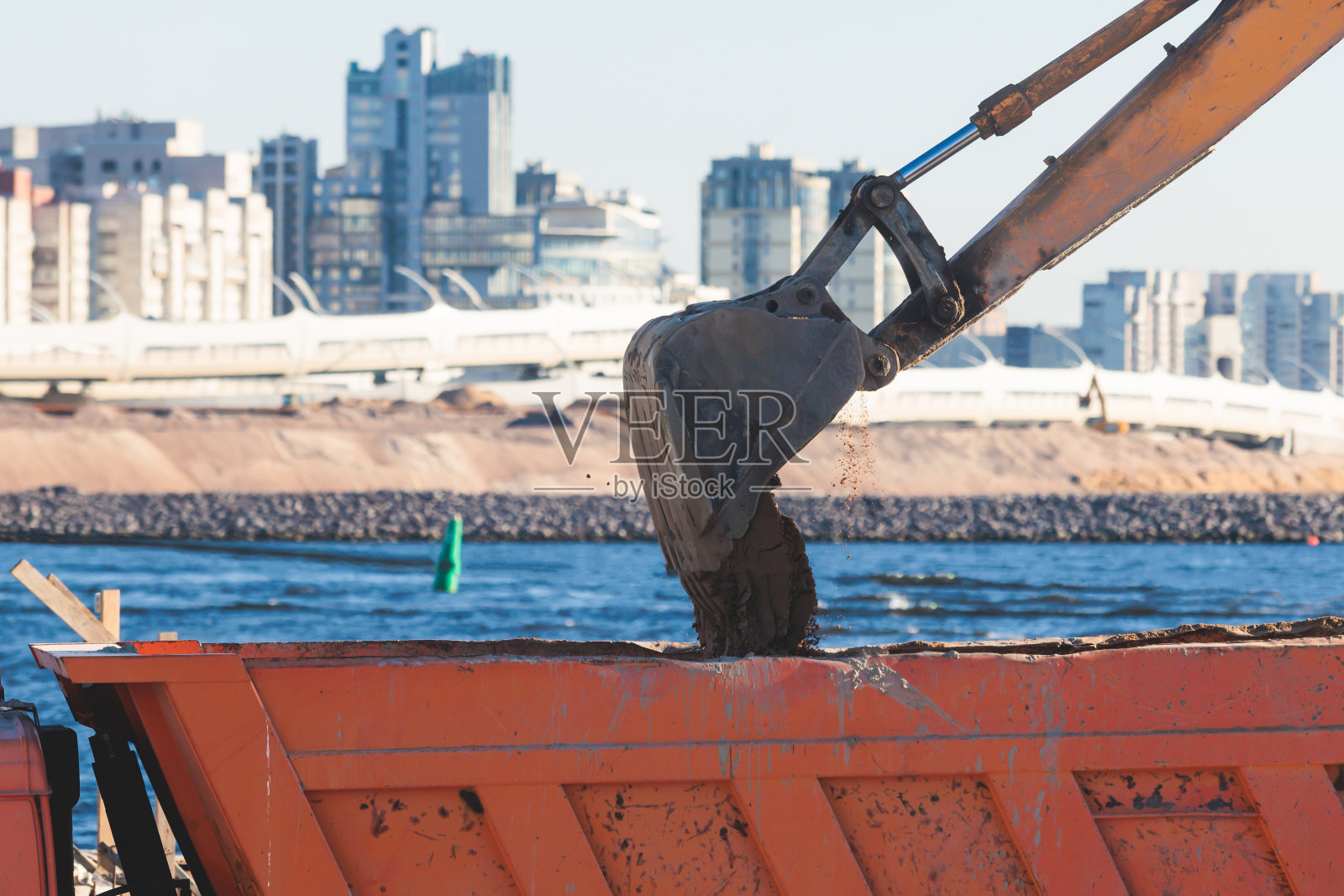 挖掘机在施工现场将沙子卸入自卸车，在道路施工期间进行挖掘和工作，反铲和自卸车卸载道路金属和砾石，施工新路照片摄影图片
