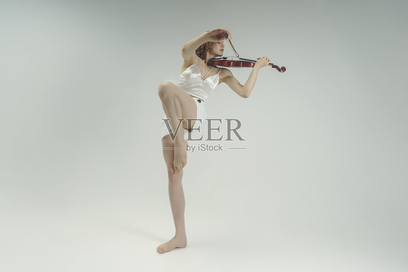 年轻的金发女音乐家单腿演奏小提琴照片摄影图片
