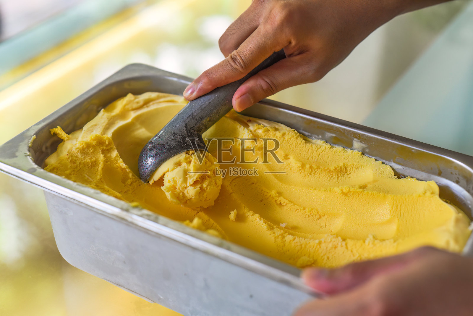 用手舀一勺百香果冰淇淋到冰箱里的勺子里照片摄影图片