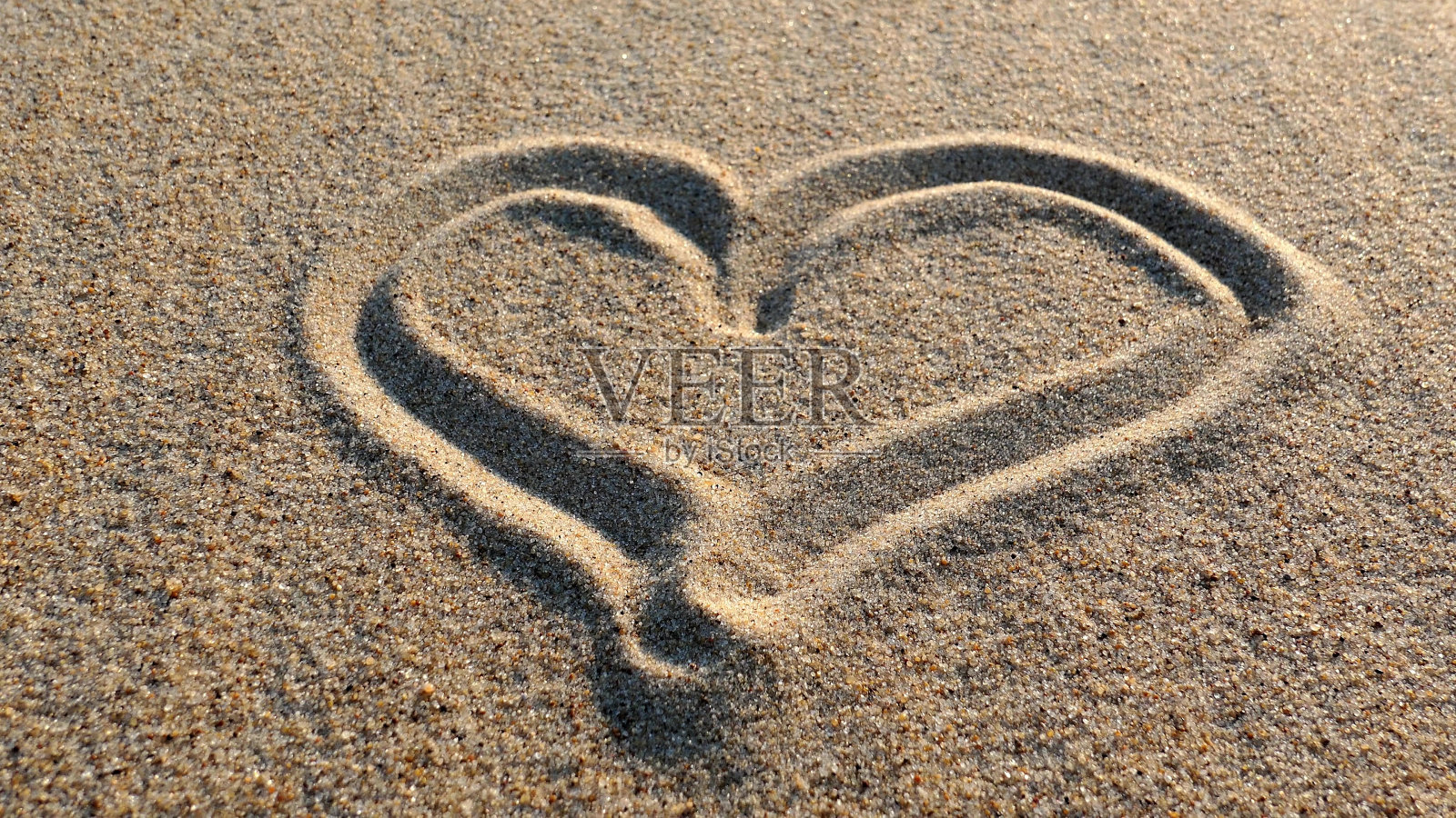 日落时分用木棍在沙滩上画心形照片摄影图片