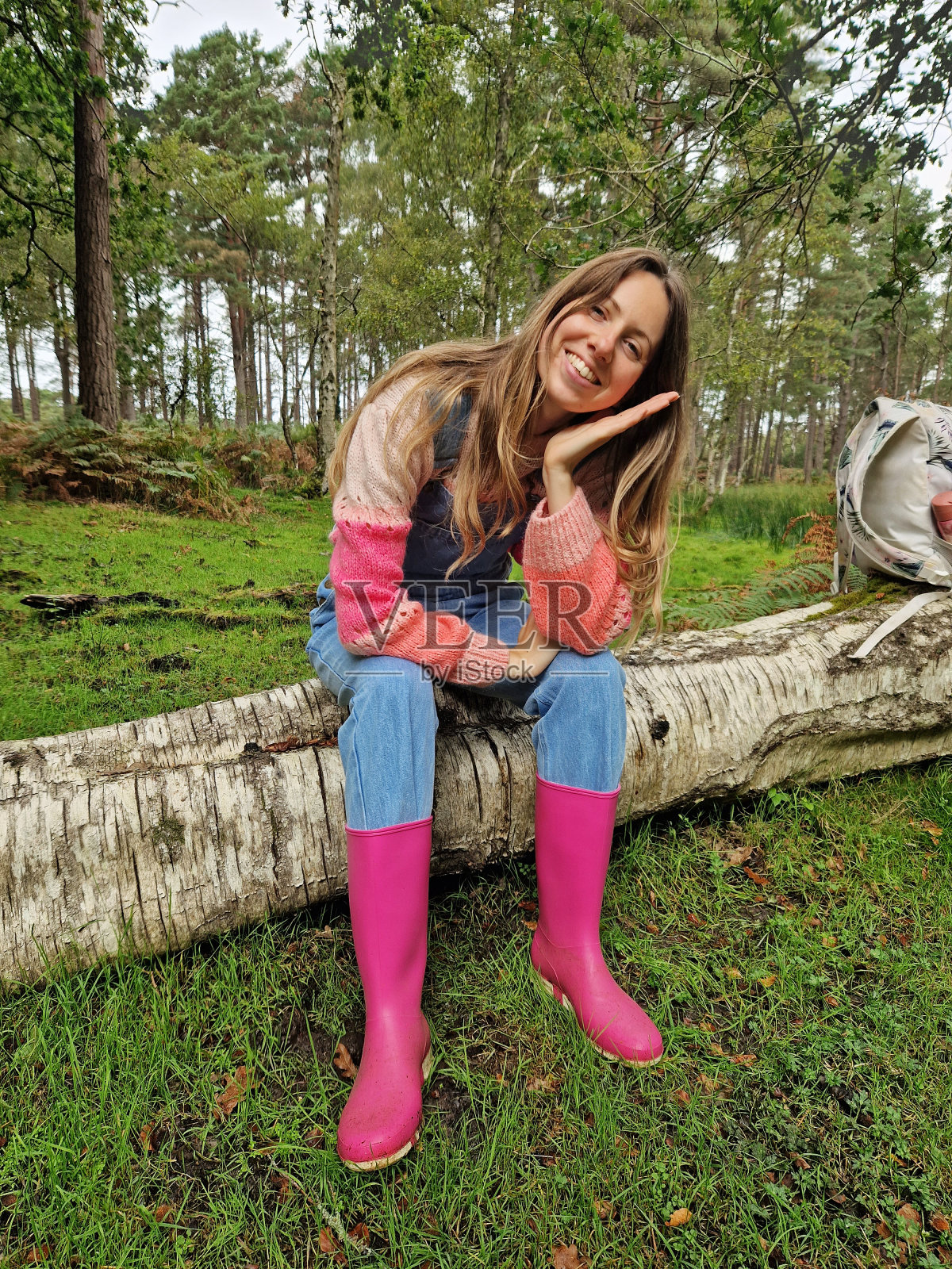 开朗的年轻女子坐在倒下的树上，穿着粉红色的靴子和工装裤照片摄影图片