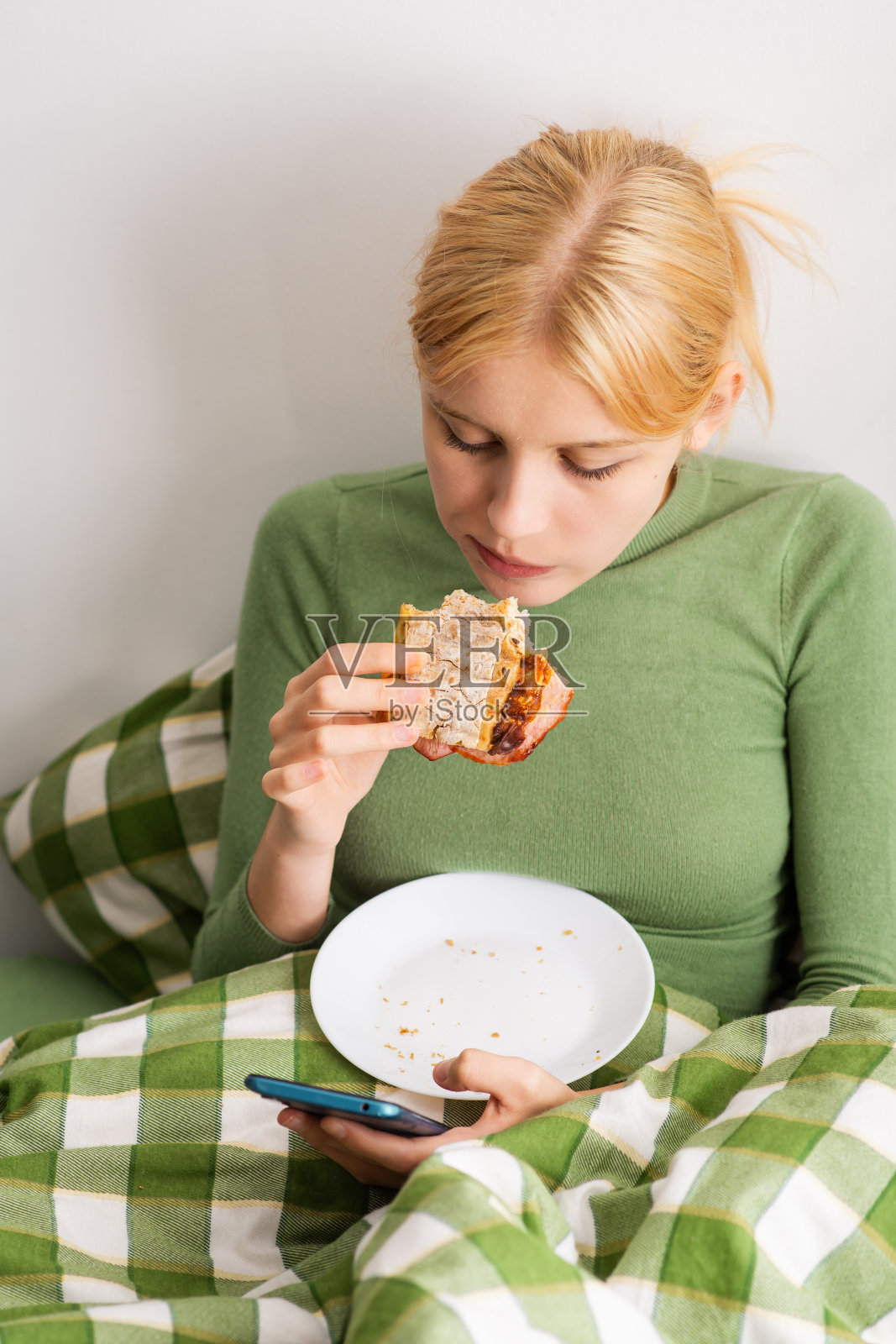 一整天，一个躺在床上的女孩经历了情绪崩溃，粘在她的手机上，吃烤面包，展示了她的精神退化。床上腐烂照片摄影图片