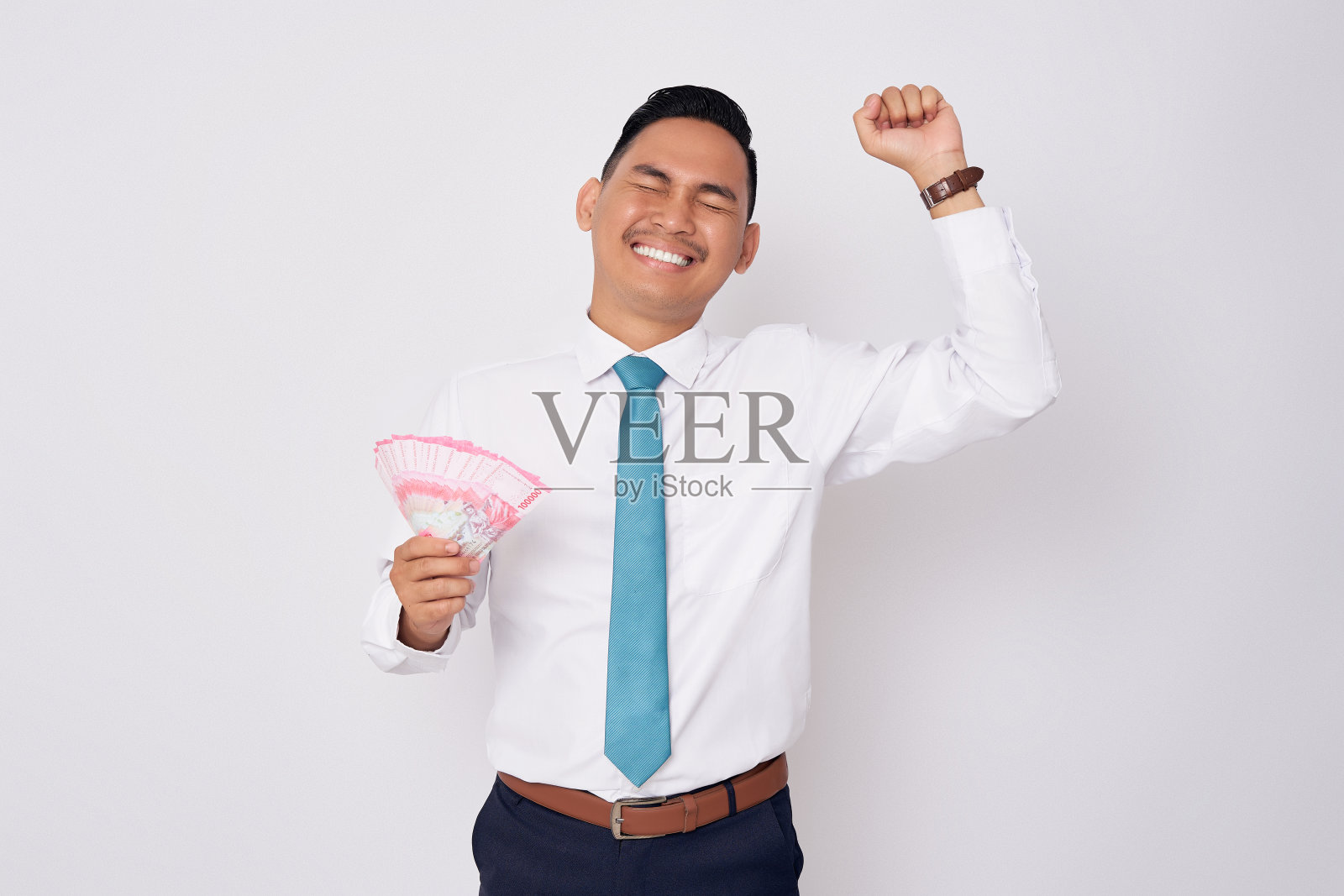 兴奋的年轻亚洲男子穿着正装，手里拿着现金，高举拳头庆祝成功，白色背景被孤立。金融与财富概念照片摄影图片