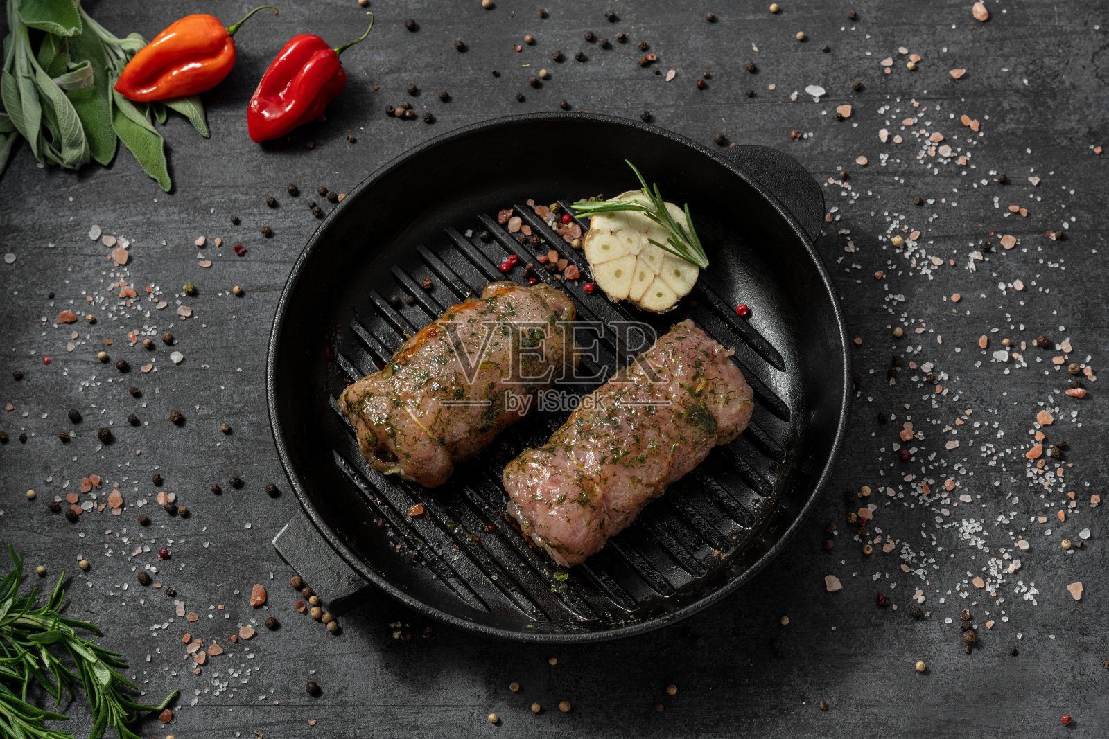 火鸡卷，奶酪，香草腌料。它躺在一个黑色的铸铁平底锅上。盘子放在深色的石头背景上，香料和草药散落在周围。照片摄影图片