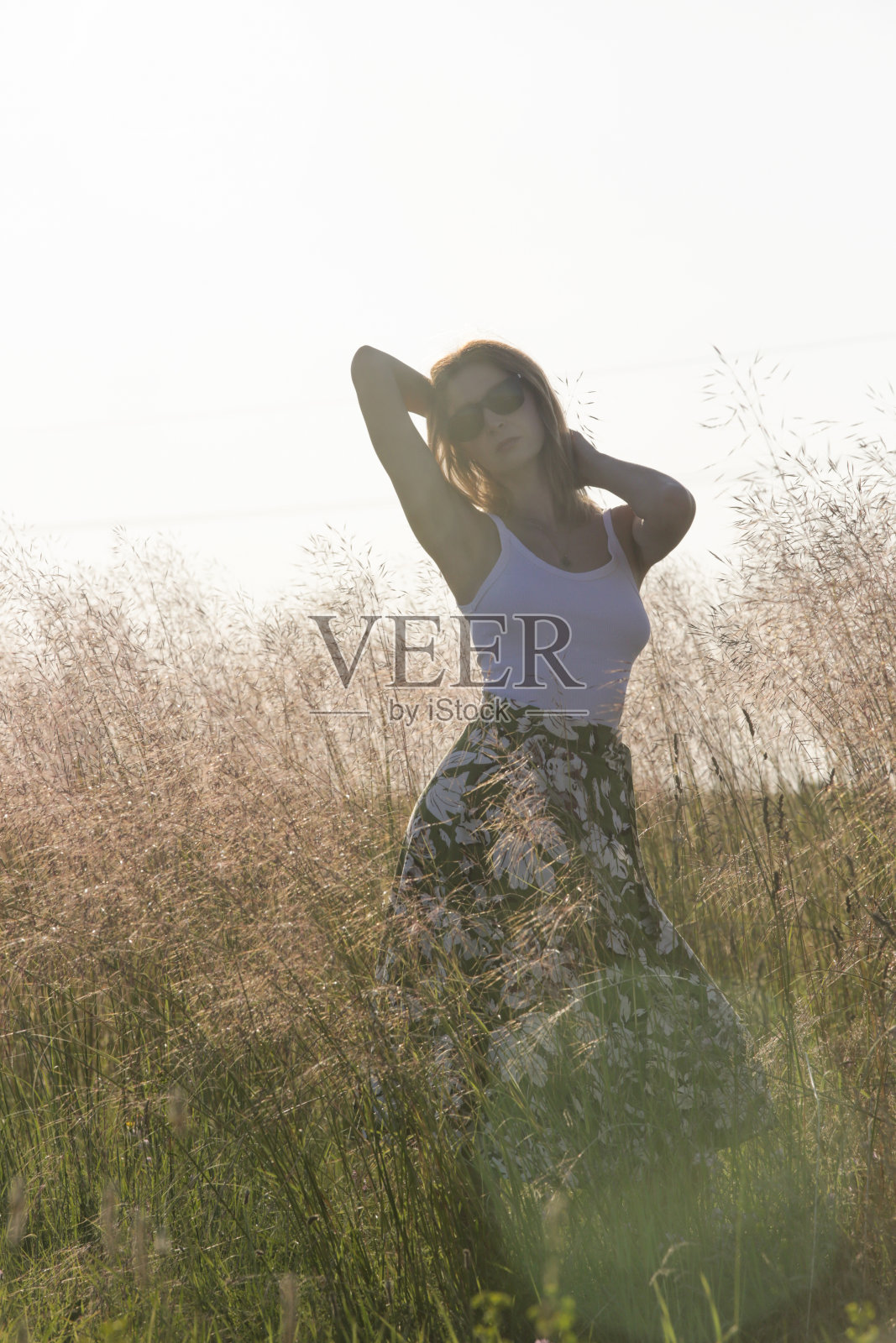 草地上年轻女子亚麻裙和白色上衣的偷拍户外肖像。夏季休闲时尚。照片摄影图片