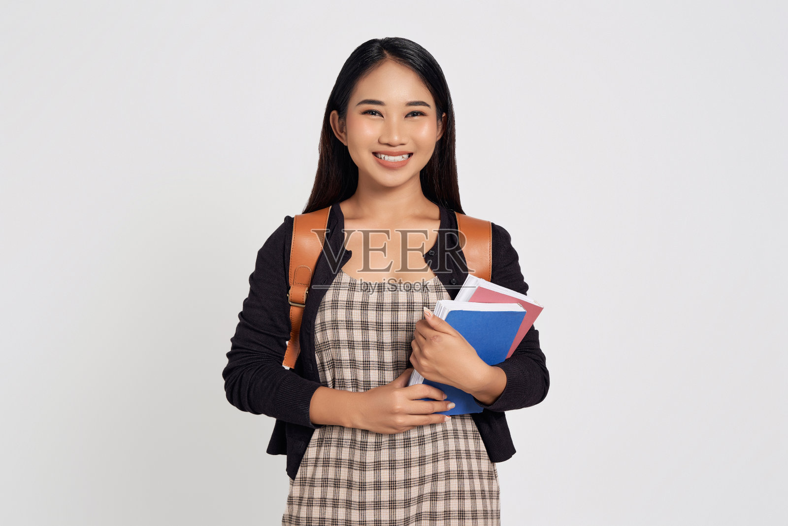 微笑快乐的年轻亚洲女学生穿着休闲衬衫和背包自信地站着，拿着书孤立在白色背景。教育在高中大学学院的概念照片摄影图片