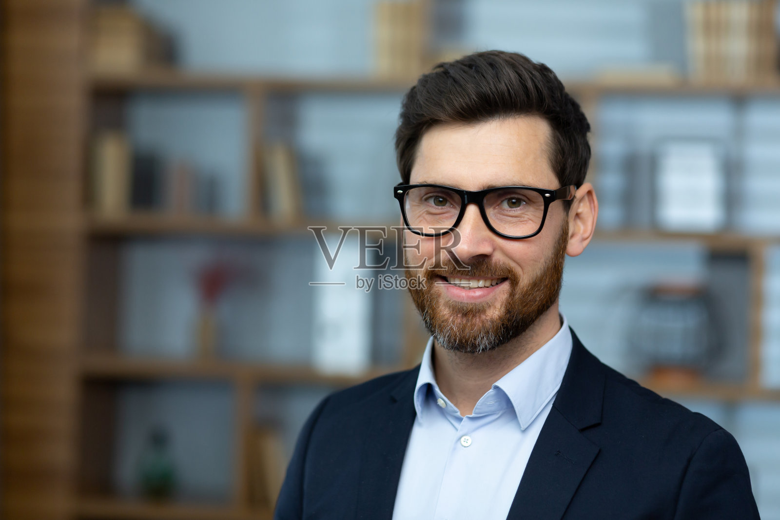 成熟的成年经验丰富的商人的特写肖像，老板微笑着看着镜头，戴着眼镜，穿着西装，成功的投资者在办公大楼内的工作场所照片摄影图片