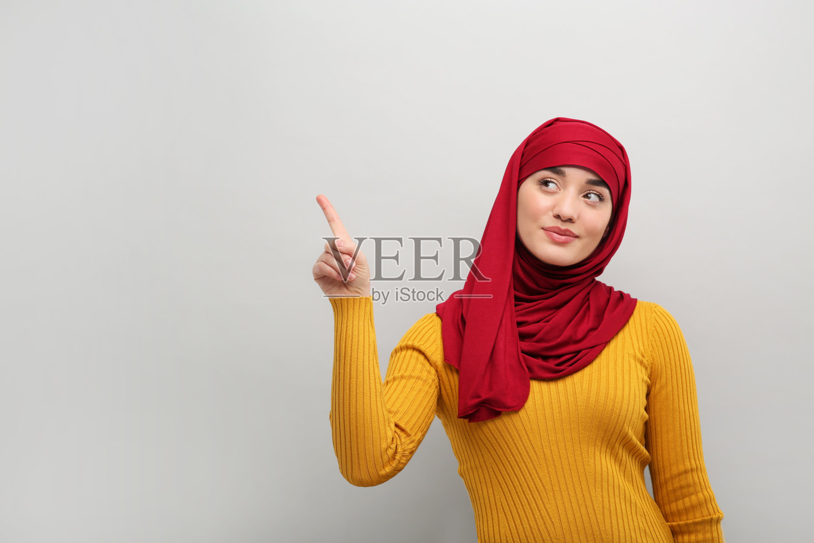 戴头巾的穆斯林妇女指着浅灰色背景上的某样东西，留出文字空间照片摄影图片