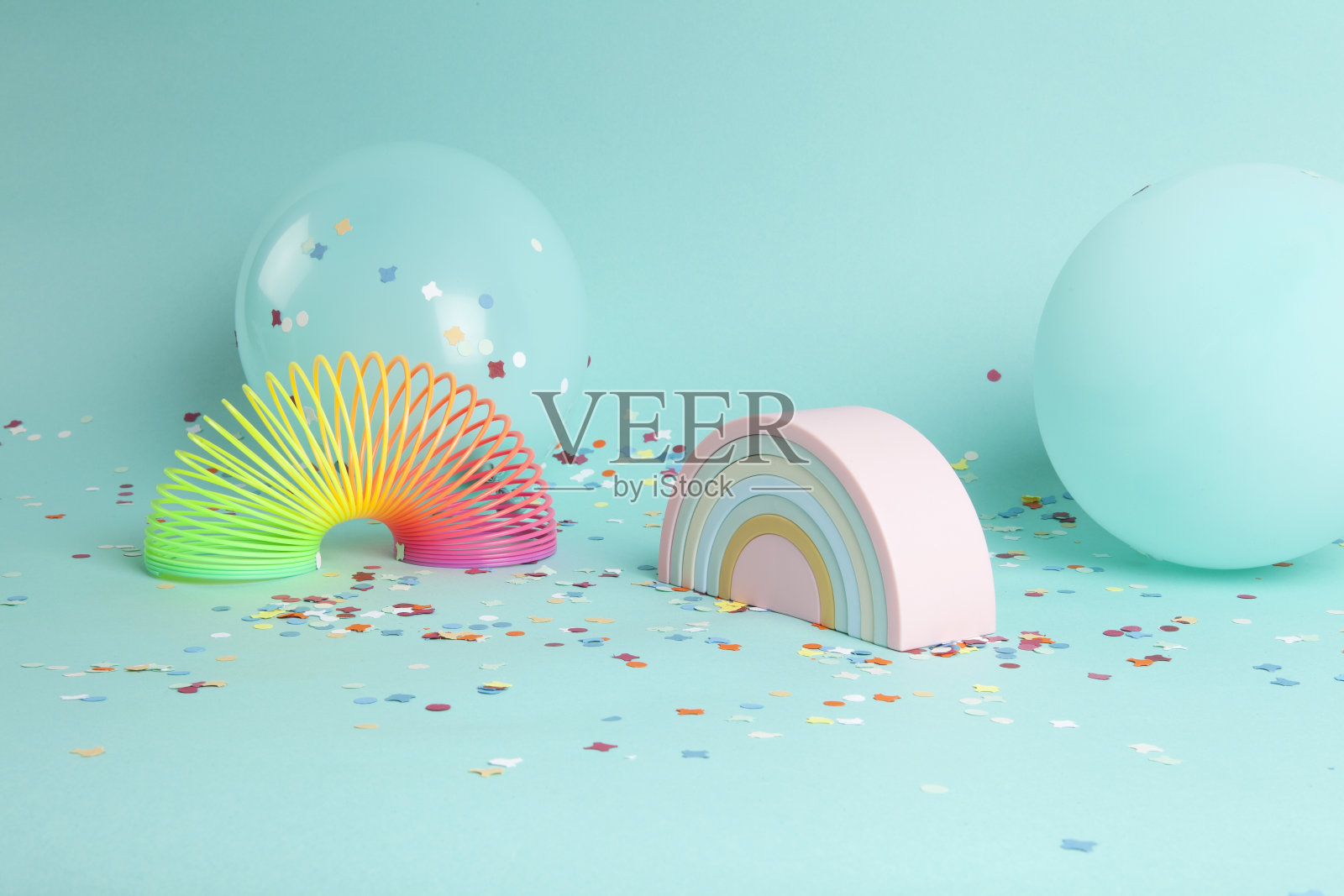 一个塑料彩虹玩具和一个与背景颜色相同的气球前面的小精灵照片摄影图片