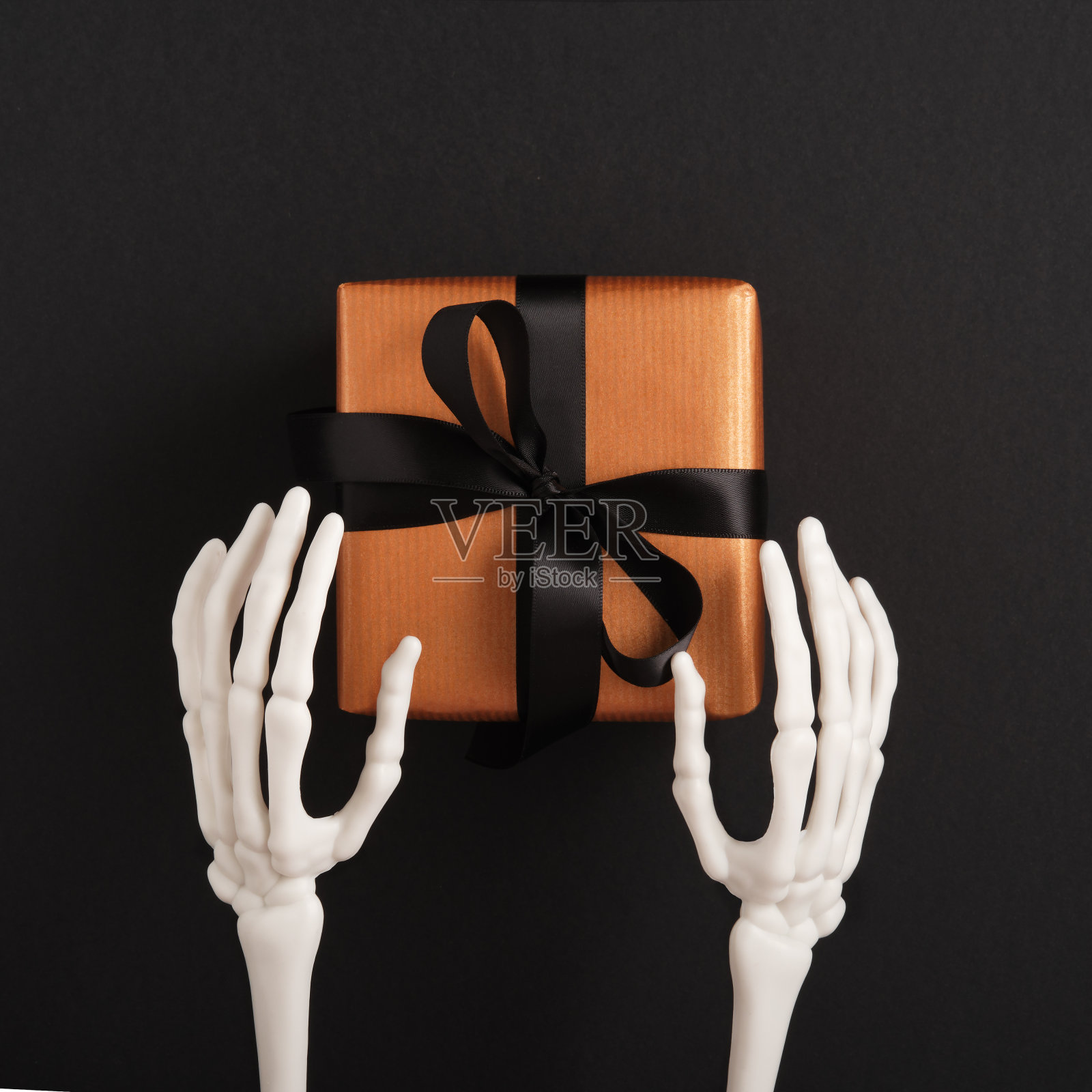 骷髅的手伸出一个橙色的礼物，上面系着一条黑丝带。万圣节快乐。照片摄影图片