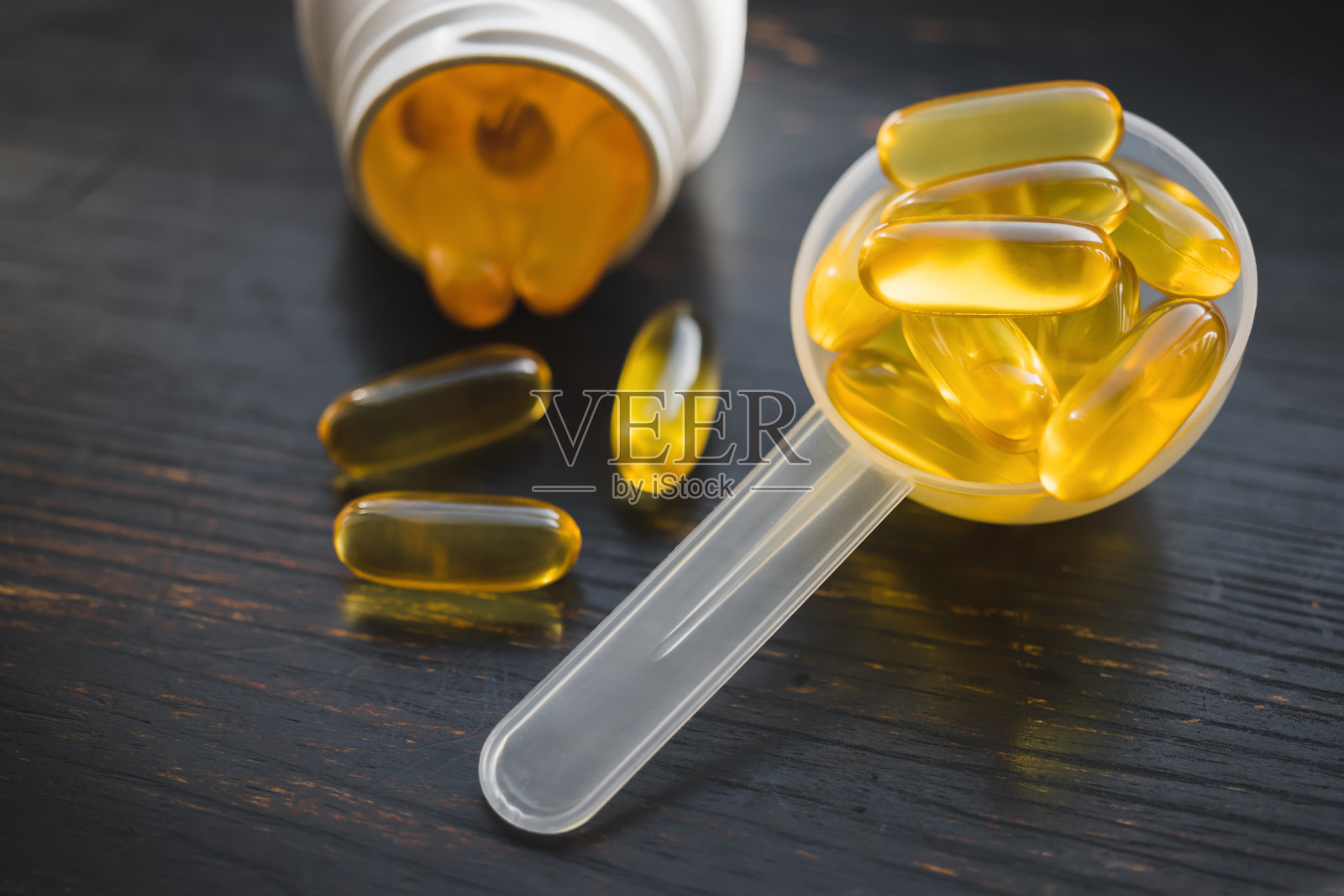 欧米茄3鱼油黄色胶囊装在塑料量勺里，膳食补充剂放在深色木板上，健康饮食理念，近距离观看照片摄影图片