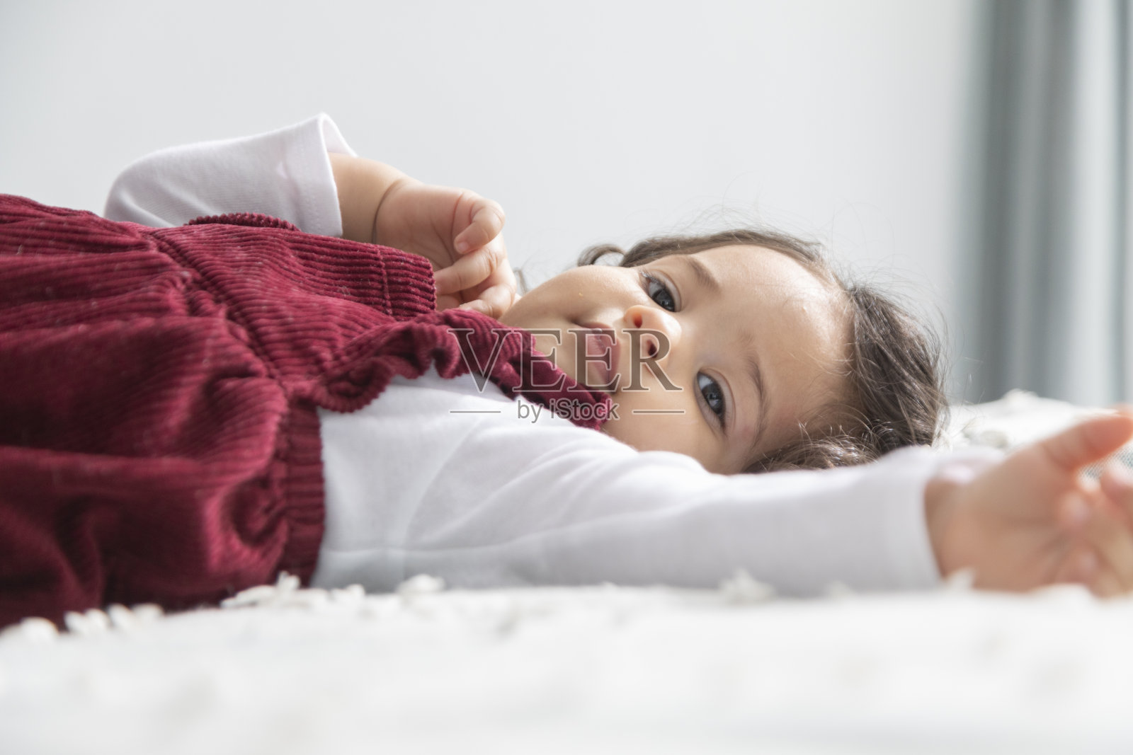 穿着红裙子的女婴躺在床上照片摄影图片