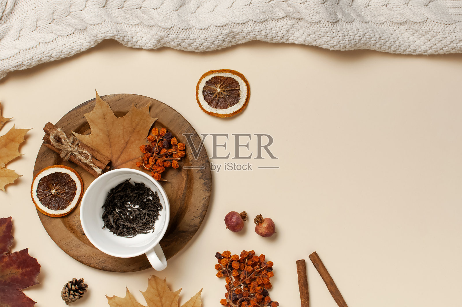 平铺秋色构图。白色茶杯配茶叶，木制盘子，针织时尚毛衣或格纹，黄色枫叶，肉桂，干山灰，米色背景上的橙色顶部视图复制空间照片摄影图片