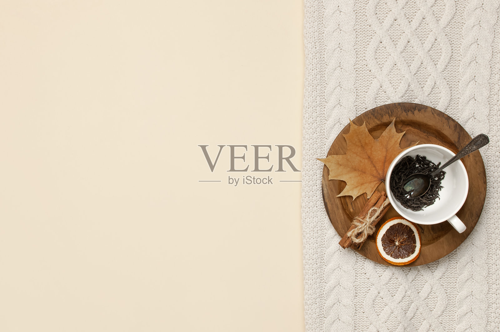平铺秋色构图。白色茶杯配茶叶，木制盘子，针织时尚毛衣或格纹，黄色枫叶，肉桂，干山灰，米色背景上的橙色顶部视图复制空间照片摄影图片