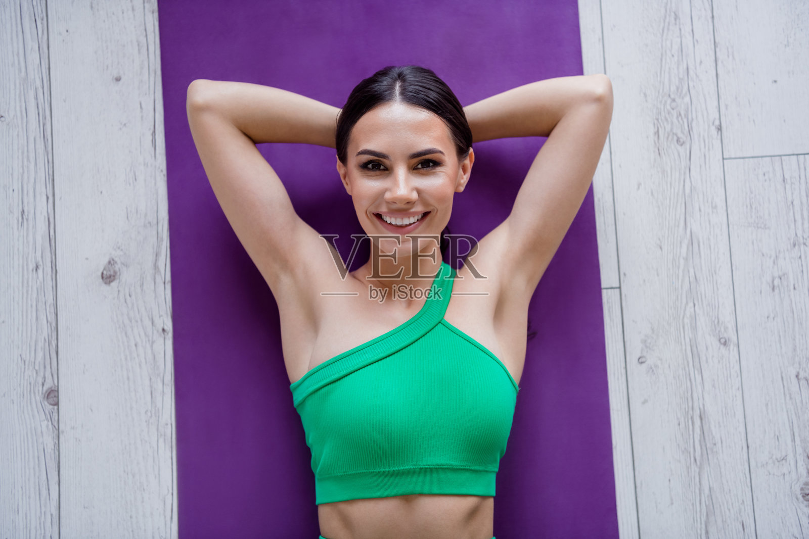 上图是非常积极的人的肖像，露齿微笑，双手放在头后，躺在健身垫上，在室内享受健身照片摄影图片