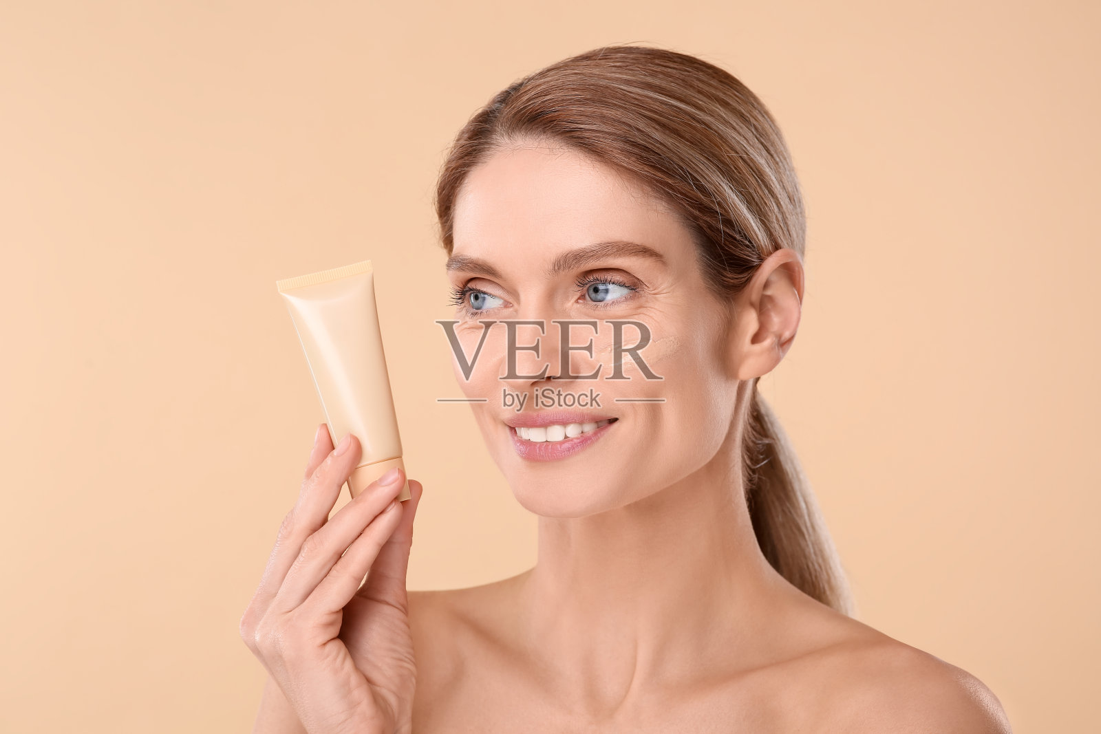 女子拿着粉底筒，米色背景照片摄影图片