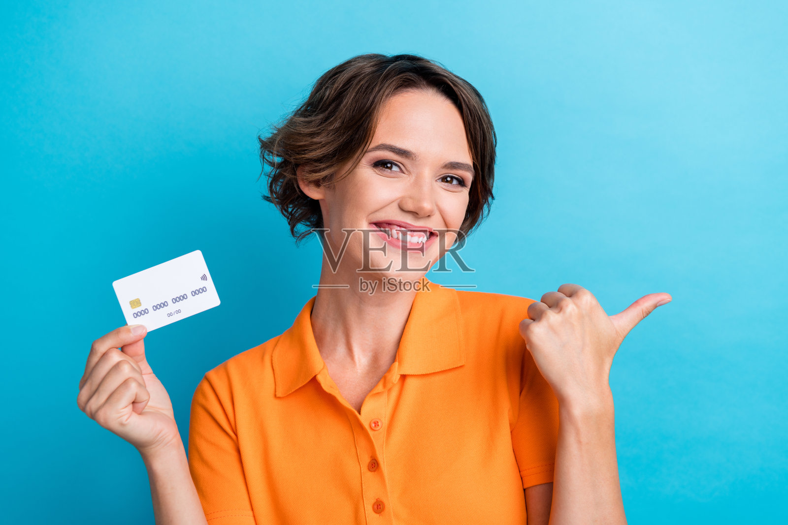 照片开朗积极的女士穿着橙色t恤上升信用卡显示拇指空白空间孤立的蓝色背景照片摄影图片