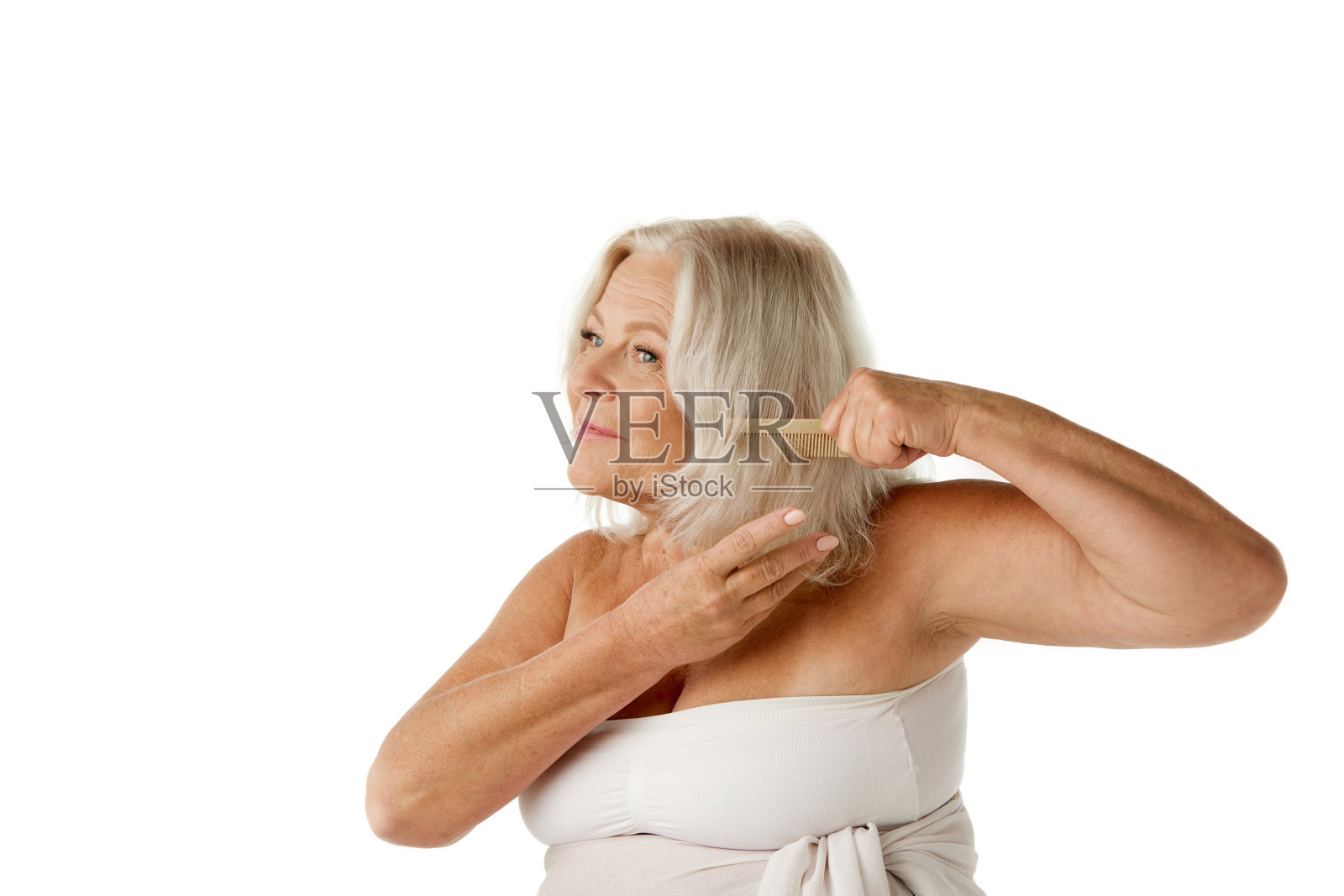 60多岁的美丽老妇人在打理头发，站在浴巾里，在白色的工作室背景下梳头照片摄影图片