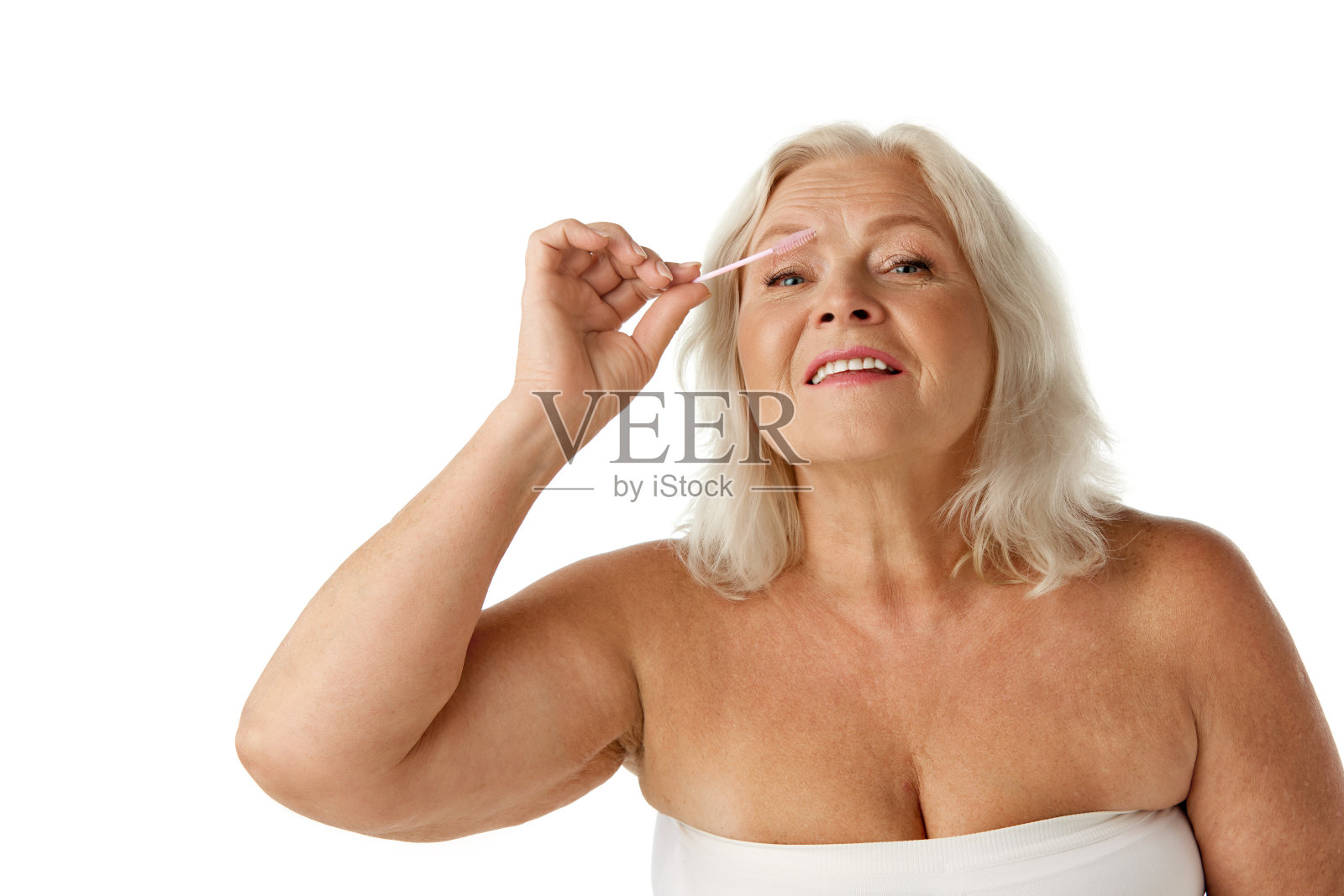 优雅、美丽的老年妇女正在打理眉毛，在白色的画室背景上用刷子刷刷照片摄影图片