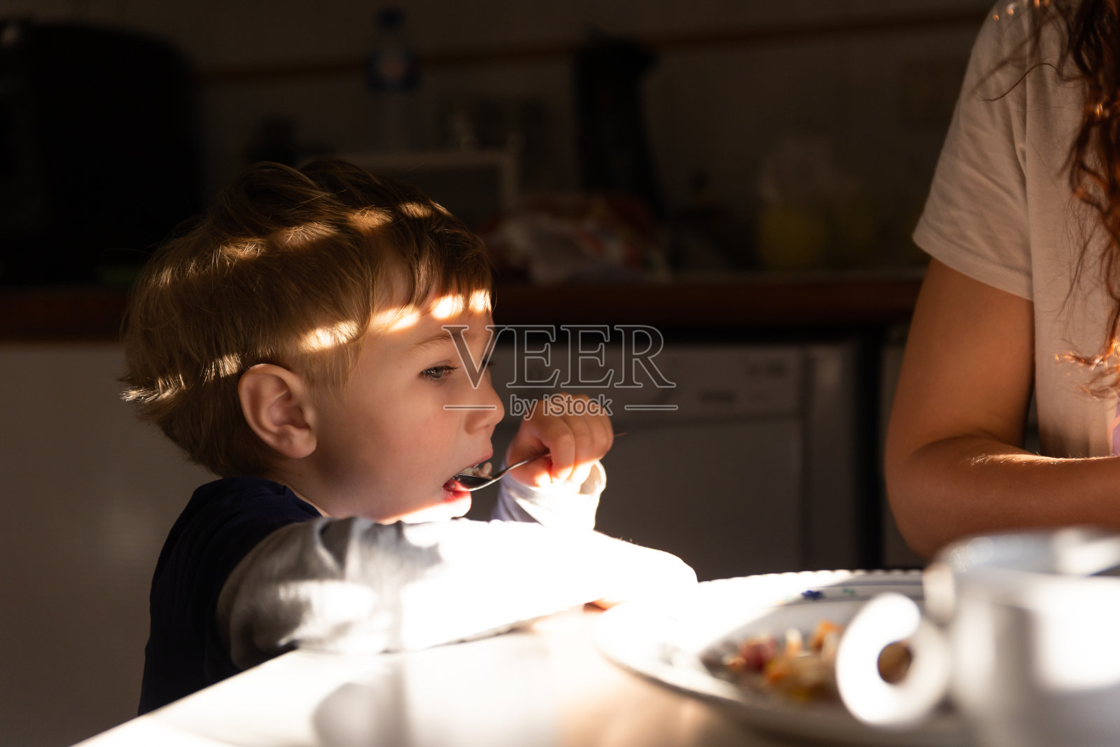 可爱的小男孩用勺子吃早餐照片摄影图片