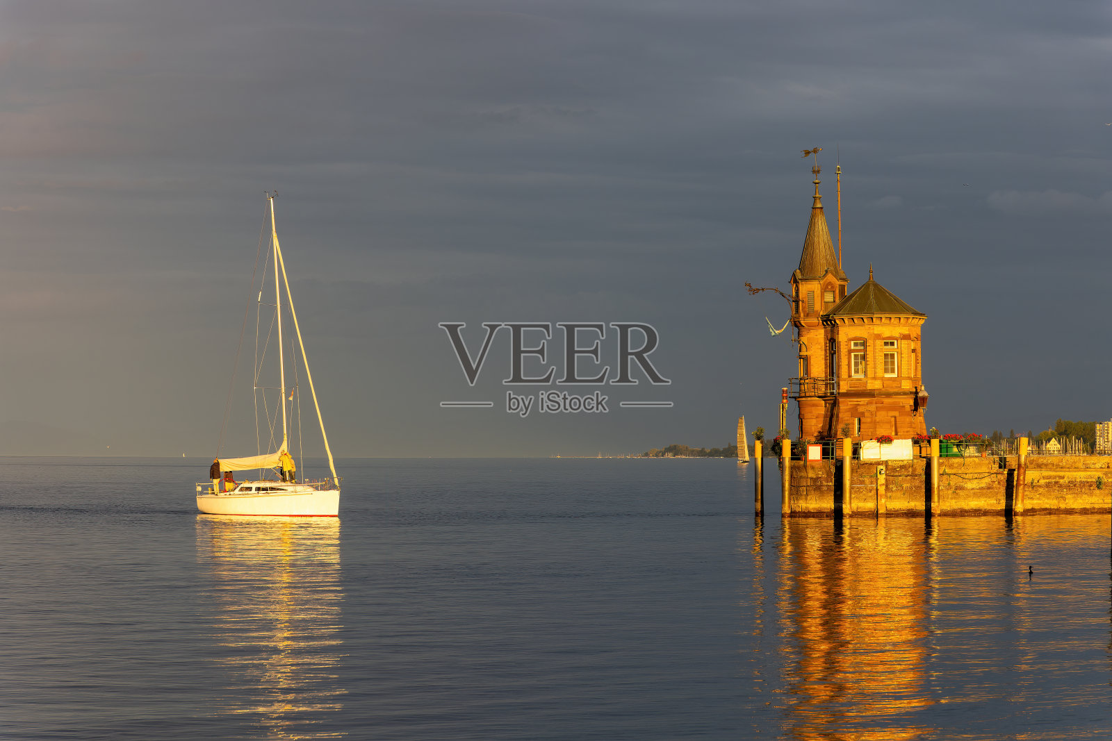 康斯坦茨在康斯坦茨湖上，海港入口处有灯塔，船只，在橙色日落中的倒影照片摄影图片