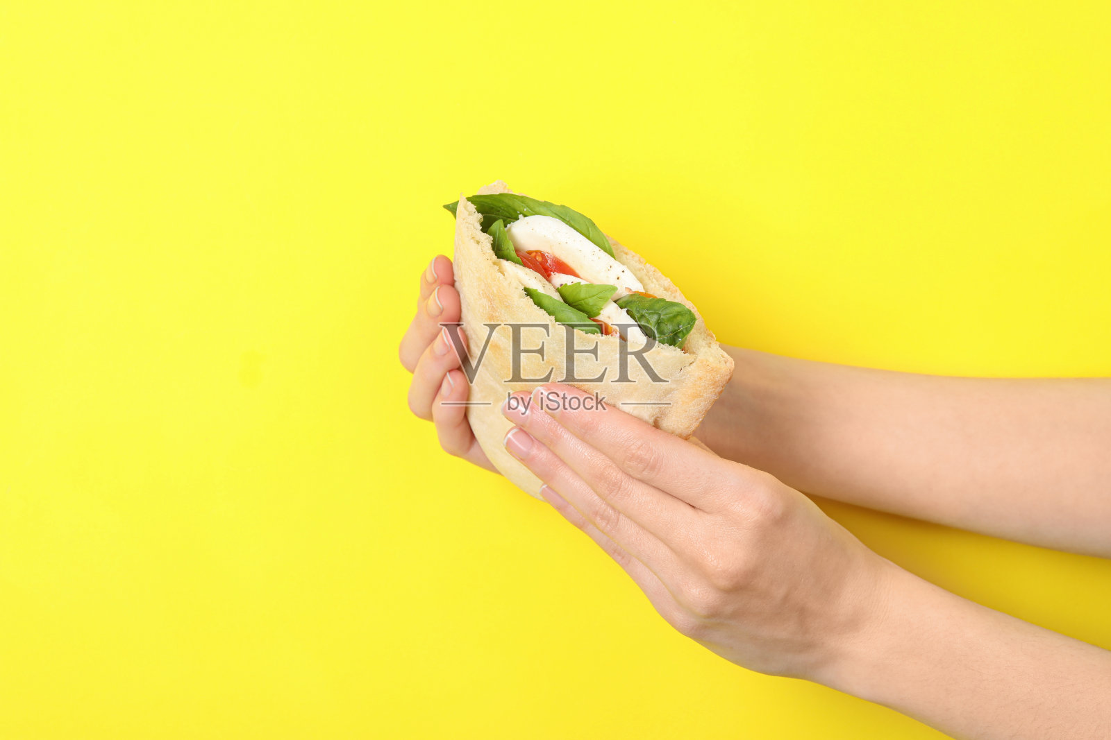 一个女人拿着美味的皮塔饼三明治，里面有马苏里拉奶酪、西红柿和罗勒(黄色背景)，特写照片摄影图片