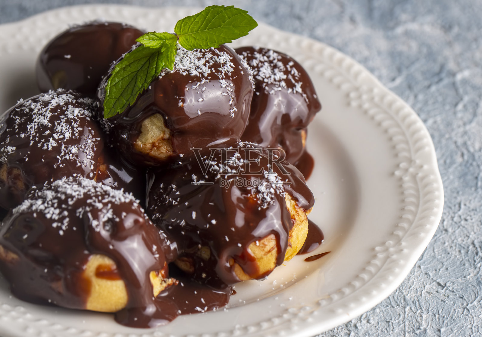 美味的巧克力泡芙和白盘子。在浅色背景上选择聚焦图像。照片摄影图片