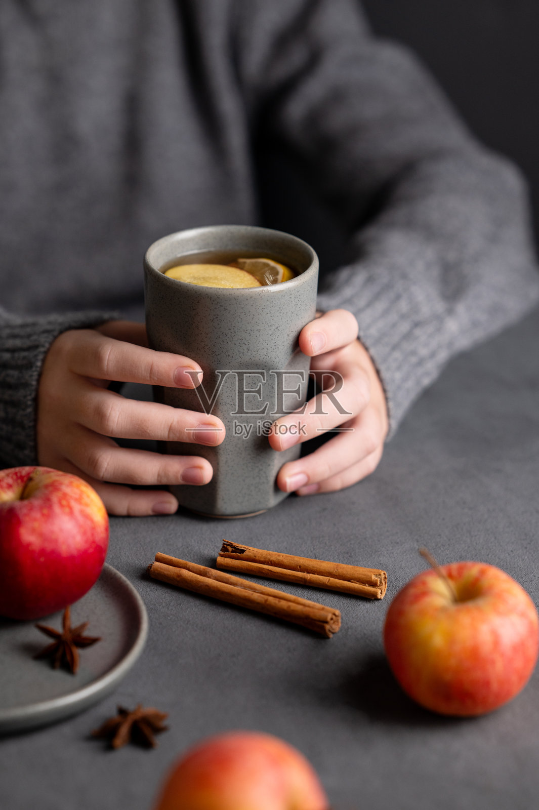 手里拿着一个灰色的杯子，里面装着自制的苹果潘趣酒或苹果和肉桂的苹果酒，暗底是新鲜的水果和香料。照片摄影图片