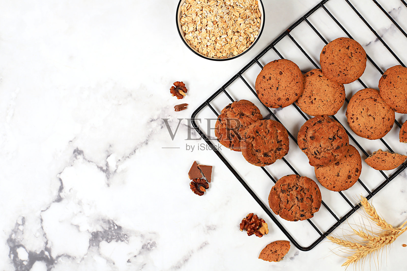 自制燕麦饼干，巧克力片和无麸质坚果放在混凝土背景上的冷却架上，现代面包店的概念是玉米穗。健康早餐配食材，俯视图，照片摄影图片