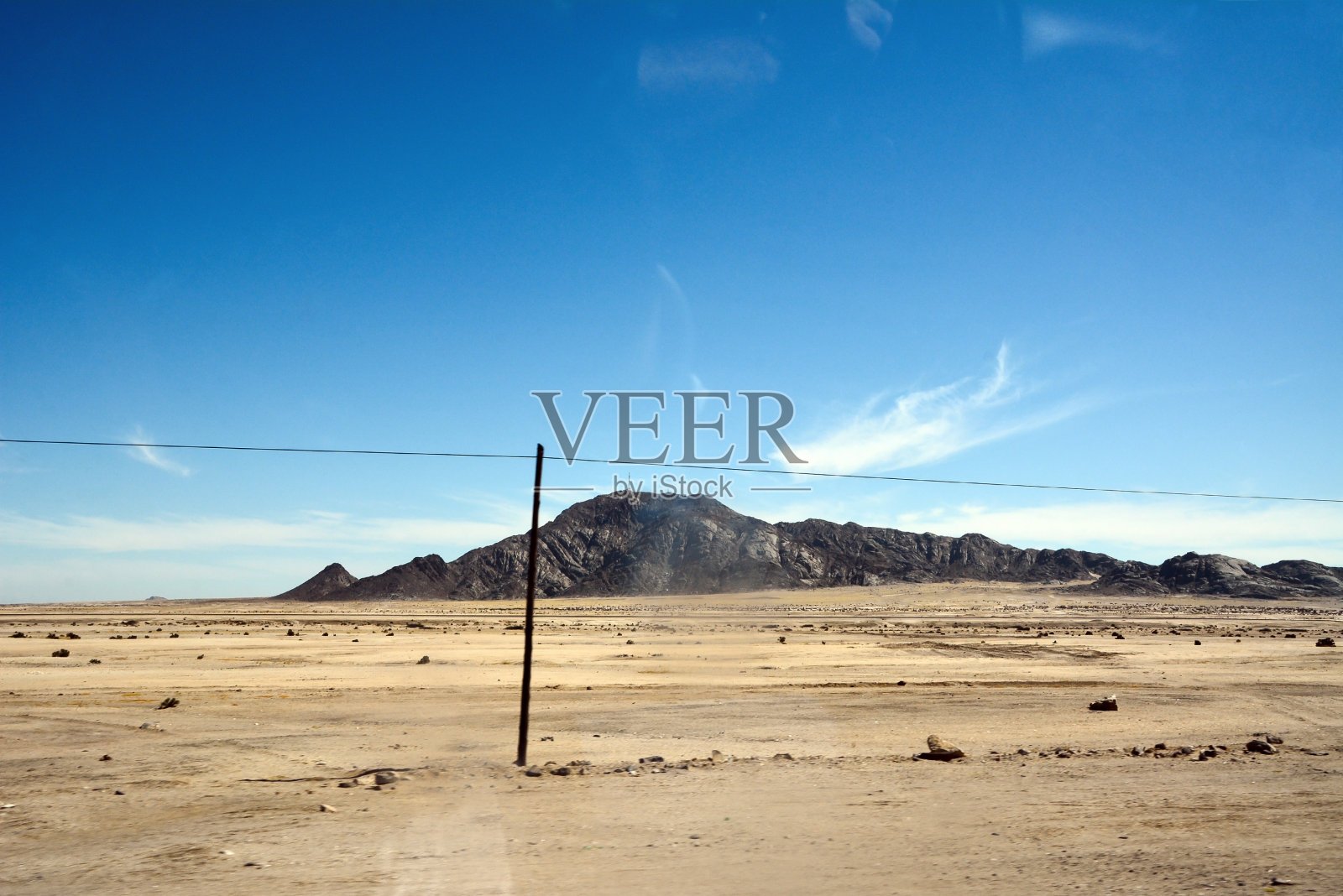 一条古老的电线穿过荒凉炎热的沙漠景观，背景是远处的群山照片摄影图片