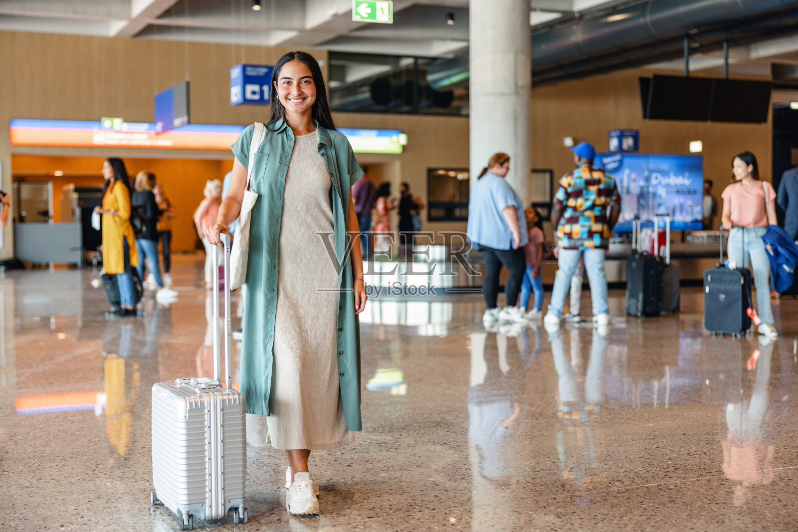微笑的年轻女子在机场拉着她的灰色手提箱照片摄影图片