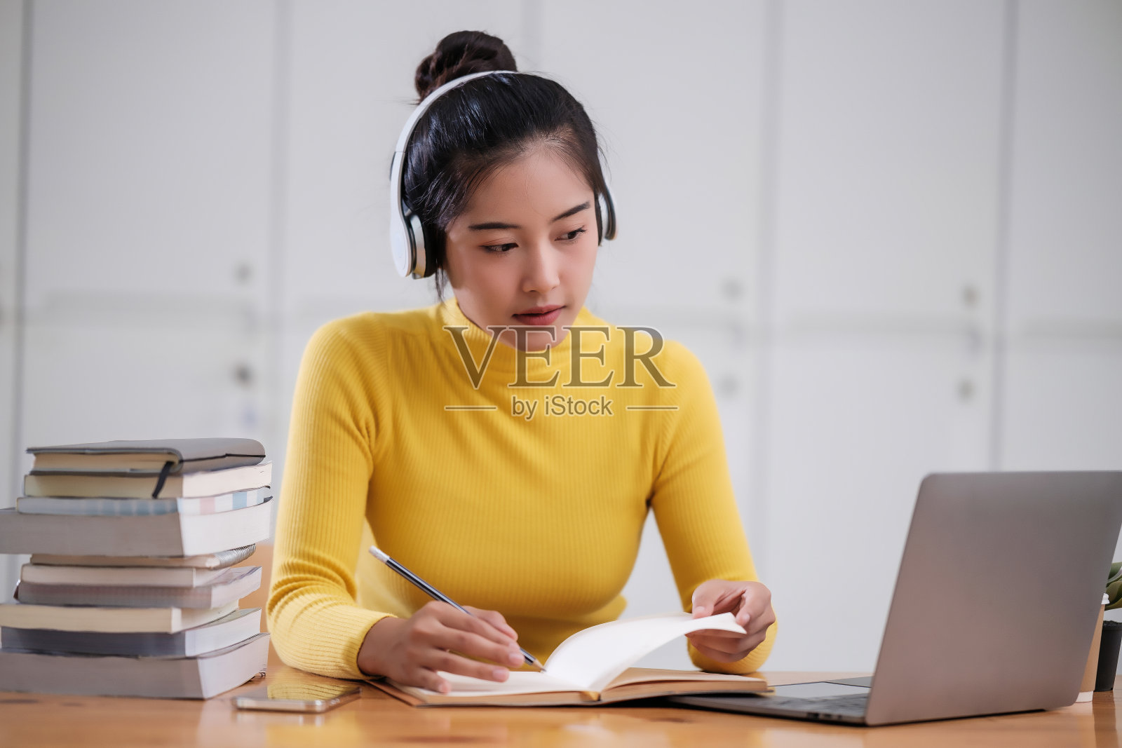 年轻的成年亚洲女学生在家里用笔记本电脑做笔记。亚洲女性在线学习听力虚拟视频通话。商业和教育理念。照片摄影图片