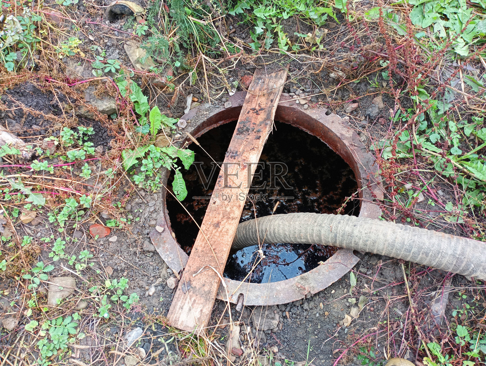 从污水中抽取污水。一个用来抽出废物的套筒被放入下水道的舱口。地下埋有一个金属桶，用来排污水。照片摄影图片