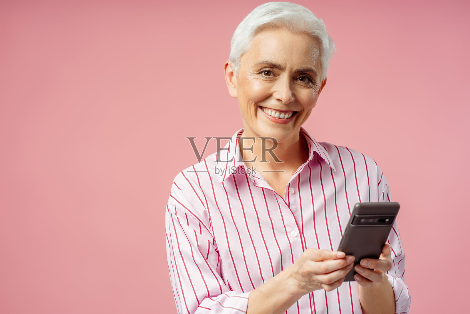 漂亮的微笑现代高级妇女拿着手机，看着相机照片摄影图片