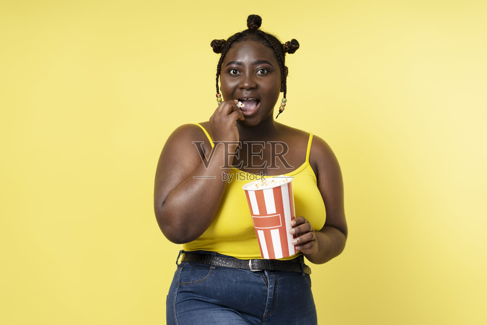 兴奋的非洲妇女的肖像吃爆米花孤立在黄色背景，模拟的地方文字照片摄影图片