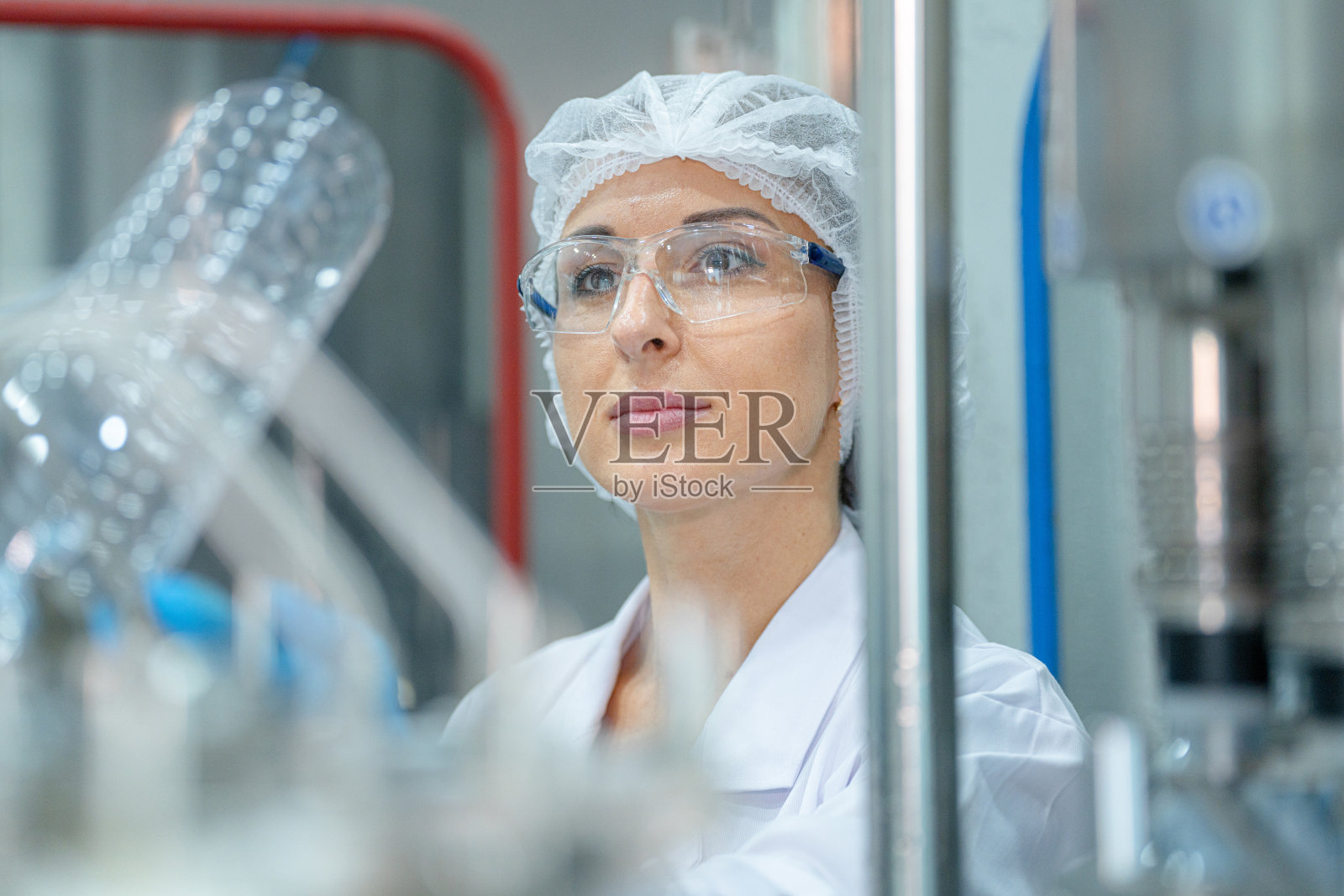 工厂女工程师检查机器上的饮水机。工人在工厂的机器传送带上检查瓶装水的质量。照片摄影图片