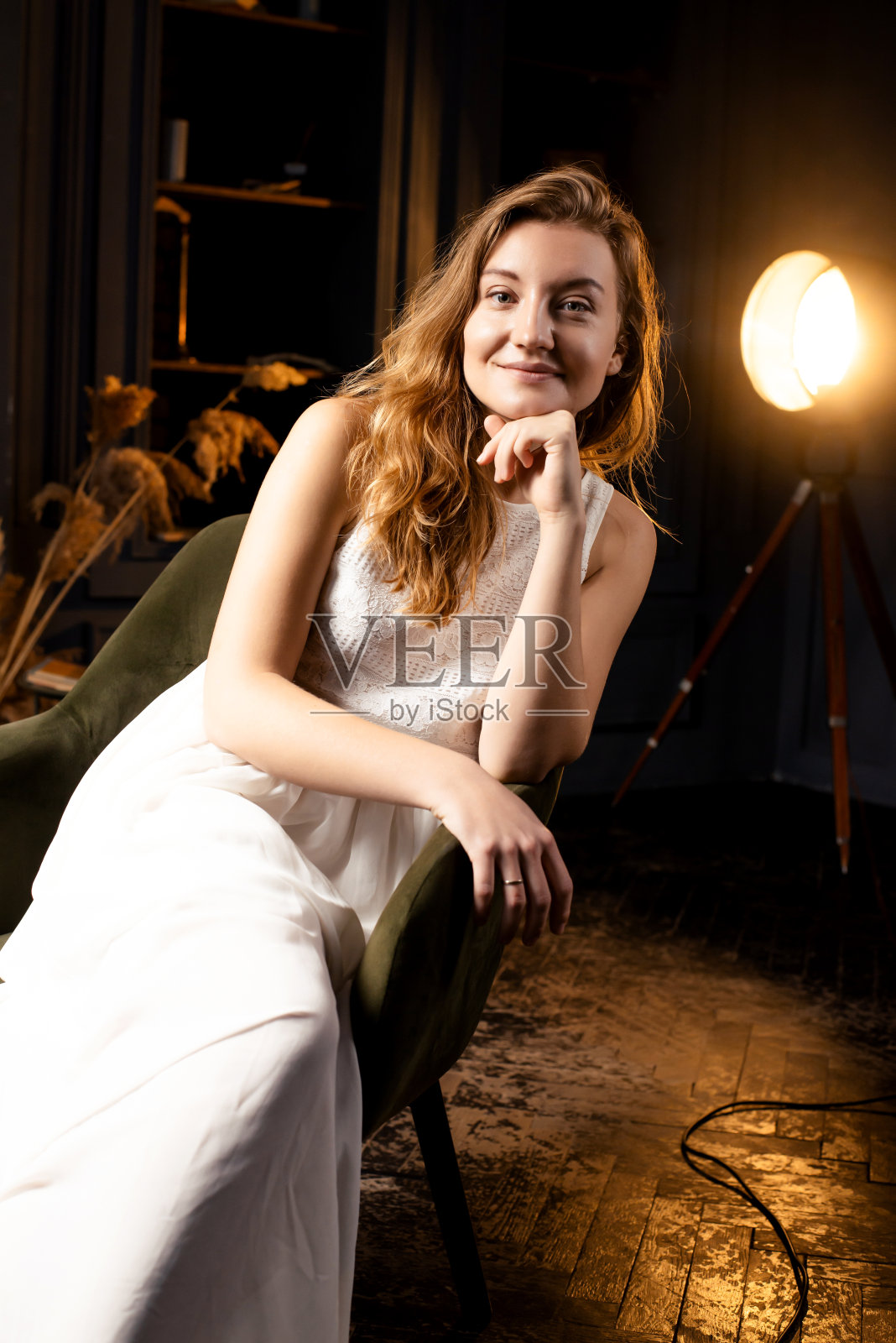 在昏暗的灯光下，一位长发飘逸的年轻女士优雅地坐在椅子上，对着镜头热情地微笑照片摄影图片