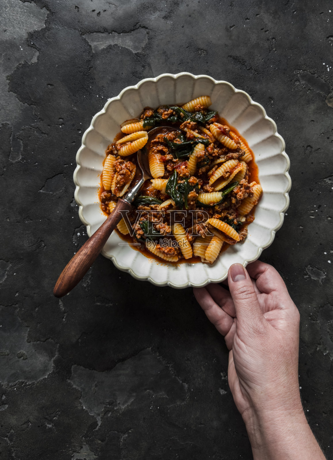 一个女人的手拿着一盘暗底的意大利肉酱面和菠菜照片摄影图片