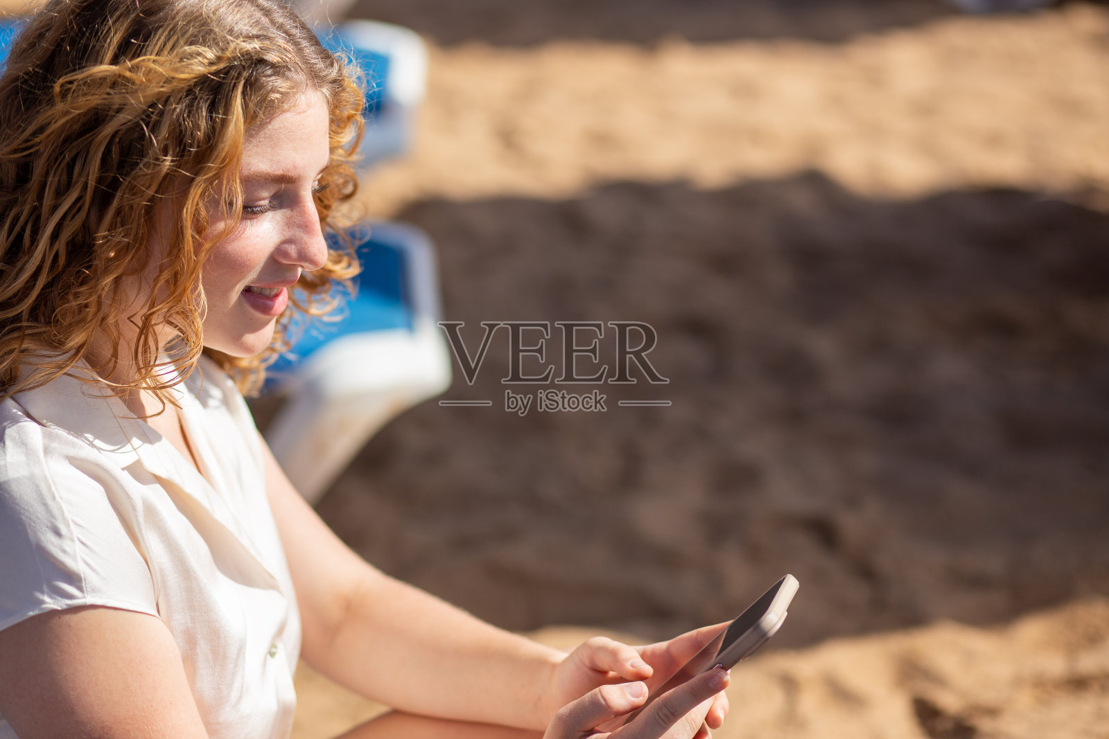 一名女子在海滩上微笑着使用智能手机。照片摄影图片