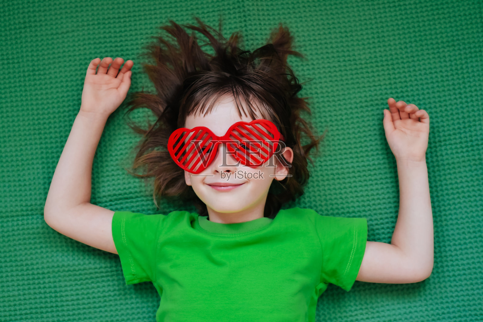 一个戴着心形眼镜的微笑女孩的肖像，背景是绿色的纺织品照片摄影图片