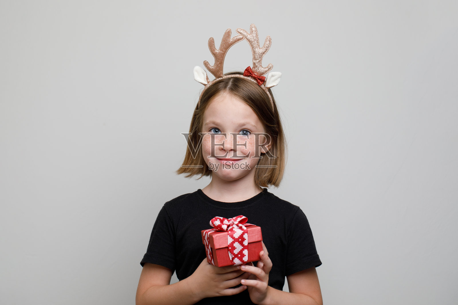 快乐的圣诞女孩在头发装饰拿着红色礼物与圣诞彩带在白色的背景照片摄影图片