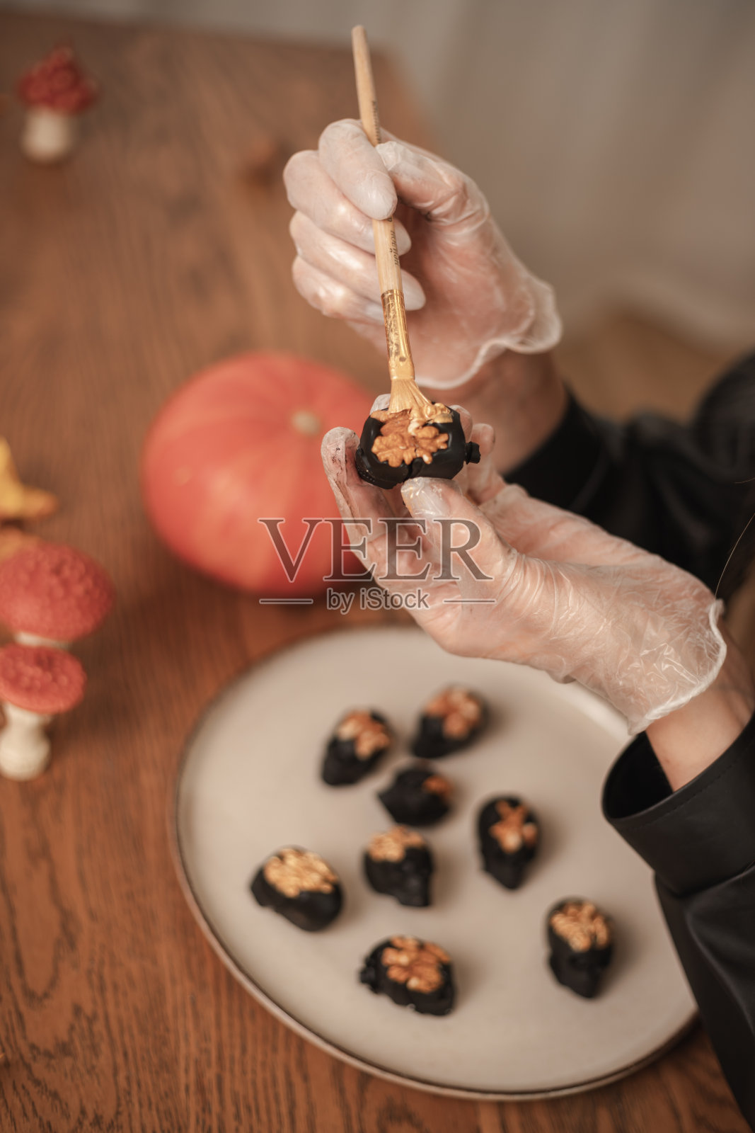 一名女糖果师在万圣节用黄金把糖果装饰成黑色头骨的形状。制作万圣节糖果的过程照片摄影图片