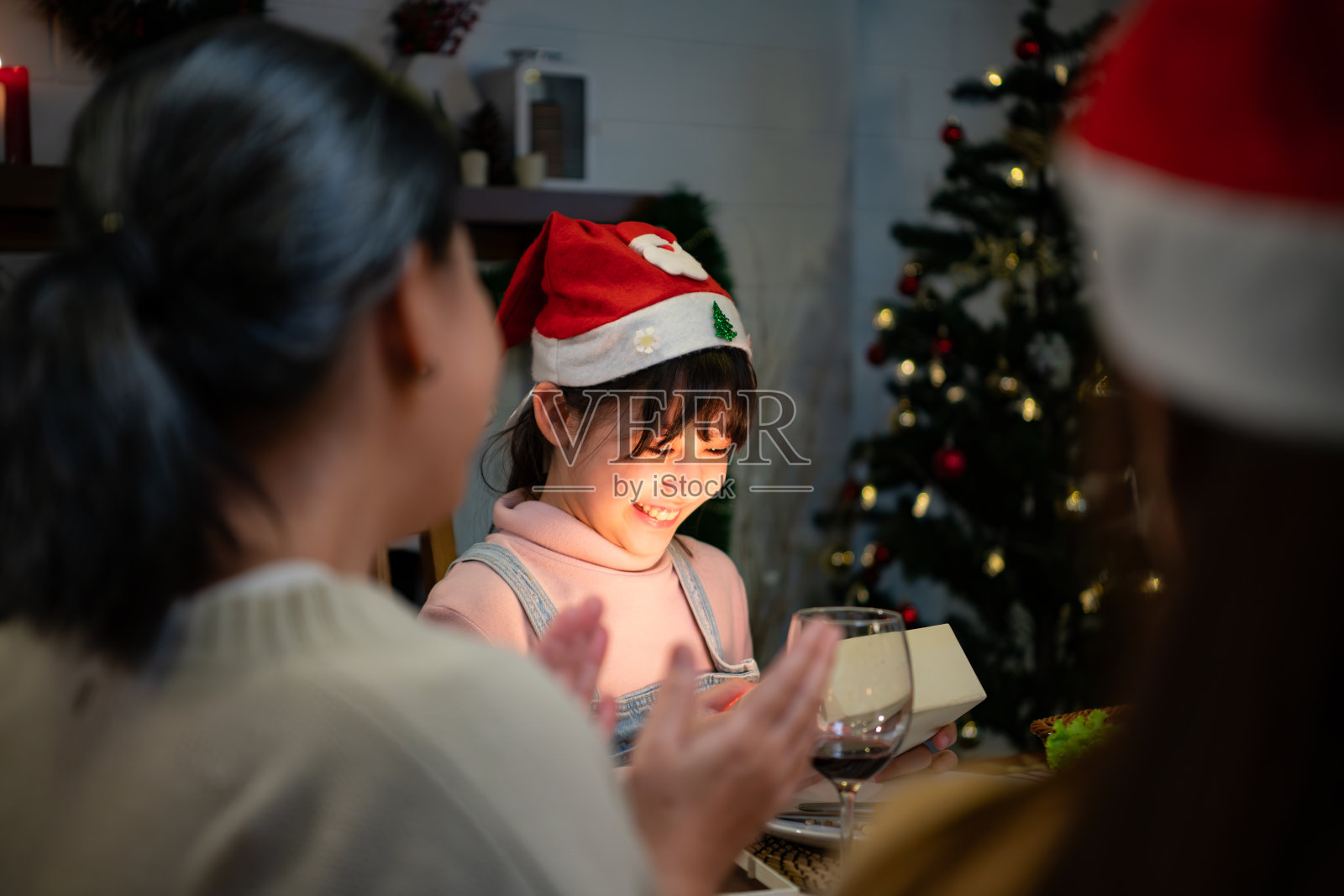 可爱的小女孩戴着圣诞帽，微笑着打开圣诞礼物。照片摄影图片