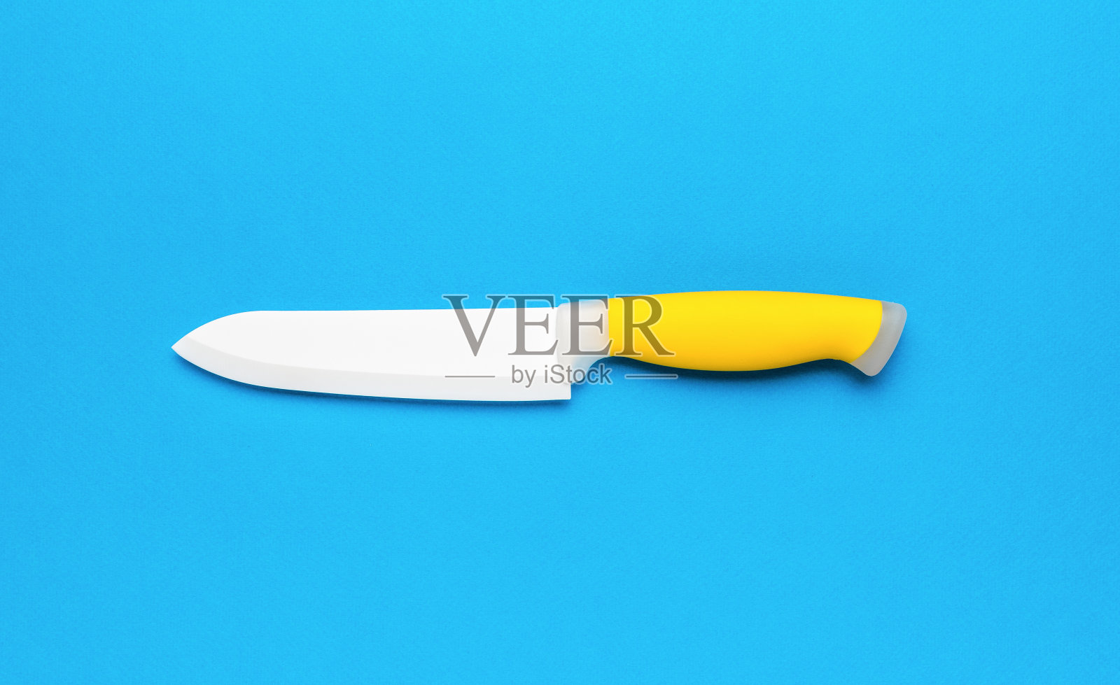 一把蓝色背景上有黄色手柄的大陶瓷菜刀。照片摄影图片