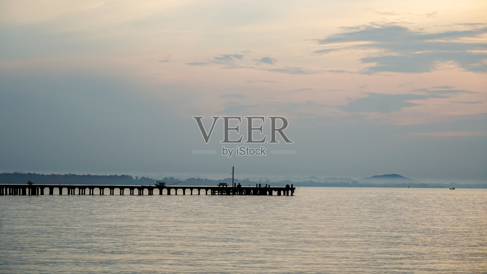 码头甲板。落日湖。紫色和橙色的天空。日落时的木码头。桥墩由木板构成，两边都有栏杆。它延伸到水中，在背景中可以看到地平线。照片摄影图片